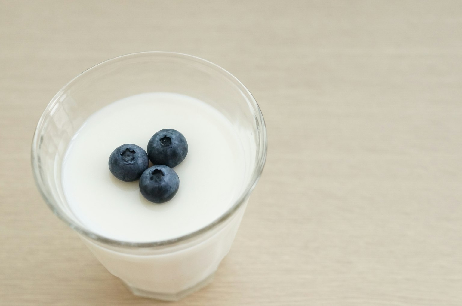 Un vaso de yogur cremoso con tres arándanos encima