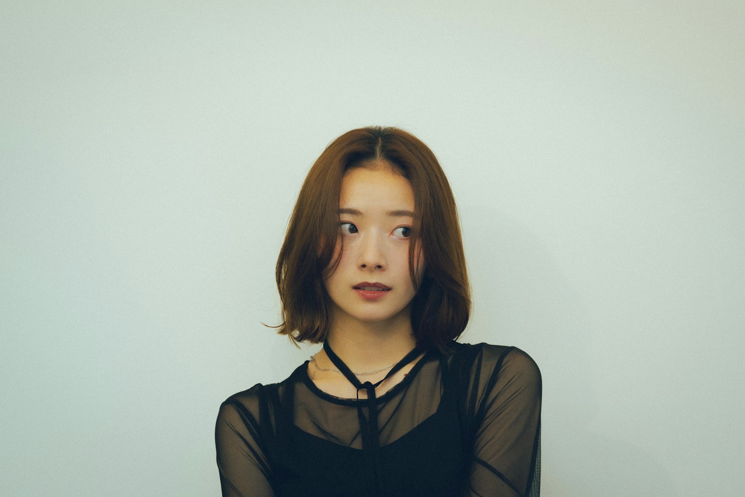 검은색 상의를 입은 젊은 여성이 흰색 배경 앞에 서 있다