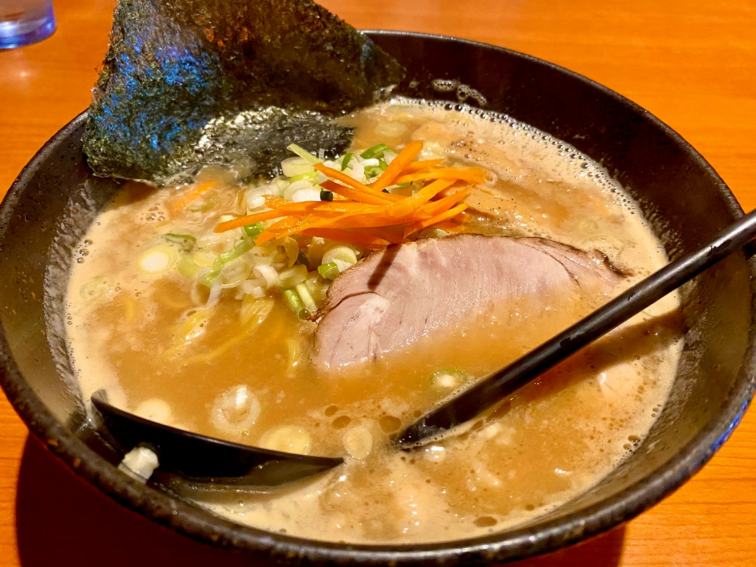 Bowl of ramen with rich broth slices of pork green onions and carrots on top
