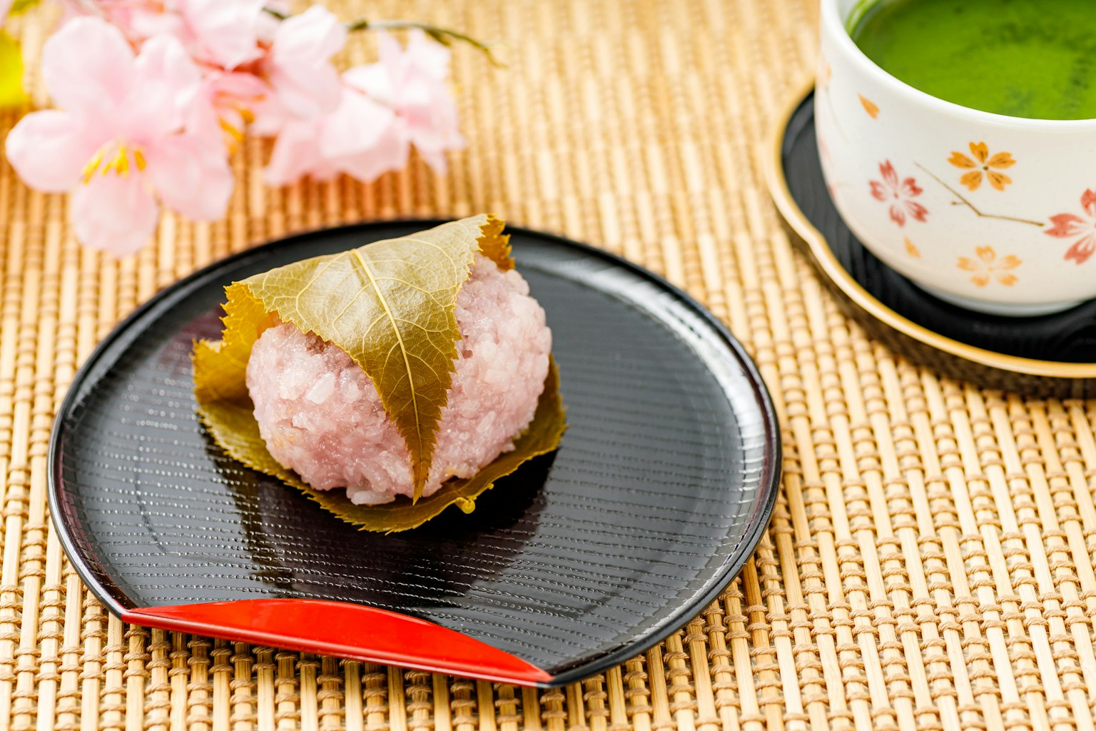 Présentation magnifique de sakura mochi à côté de fleurs de cerisier et de thé vert