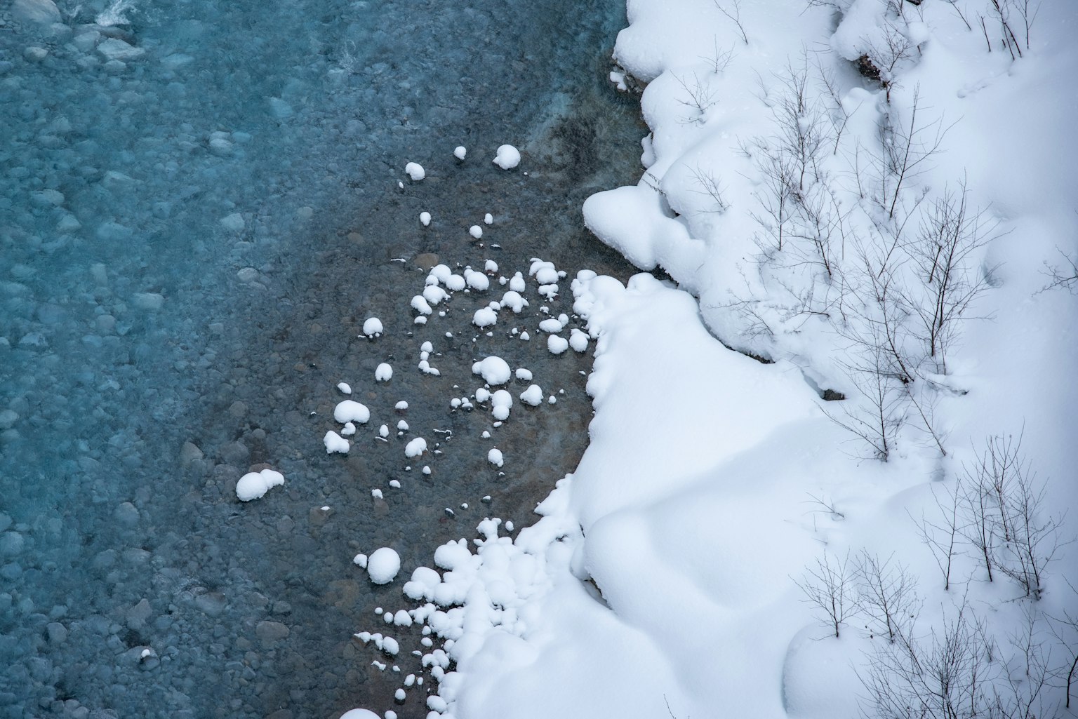 冬季風景，雪覆蓋的河岸和流動的藍色水