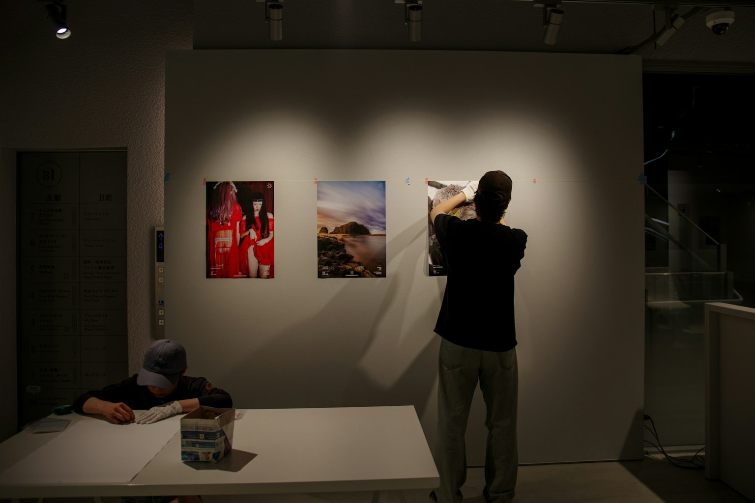 Person hanging posters in an exhibition space with art on the wall