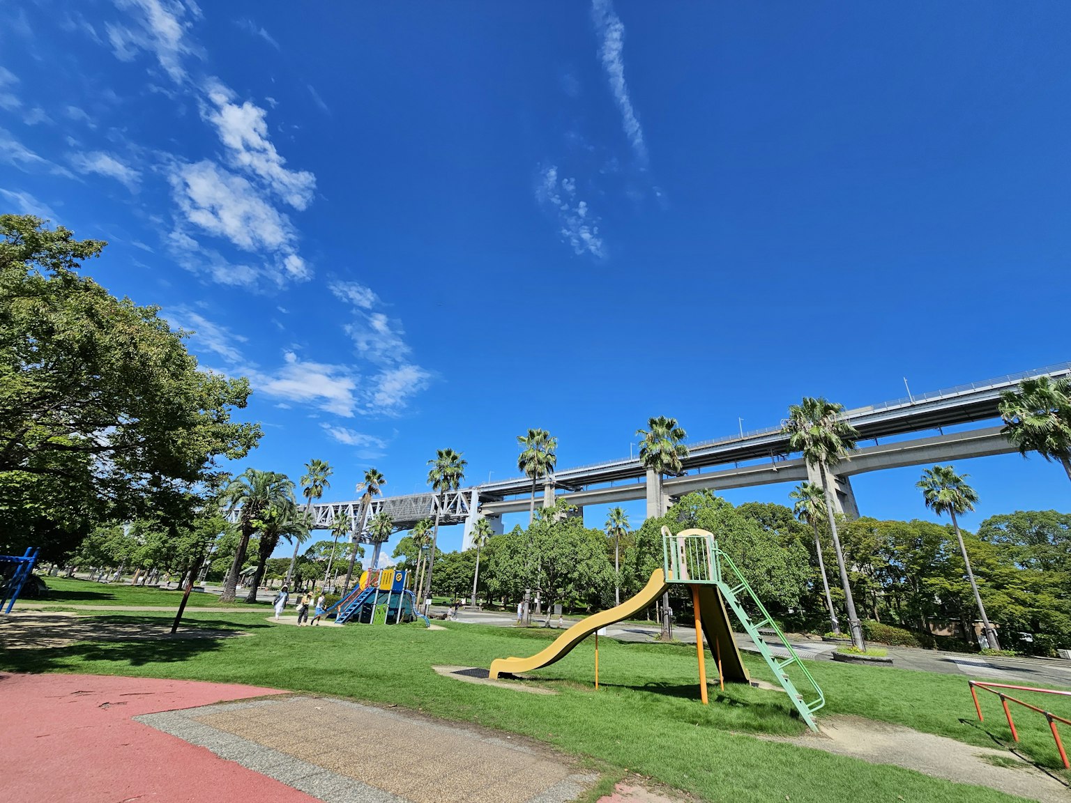 Parc avec des équipements de jeu et une voie ferrée élevée sous un ciel bleu