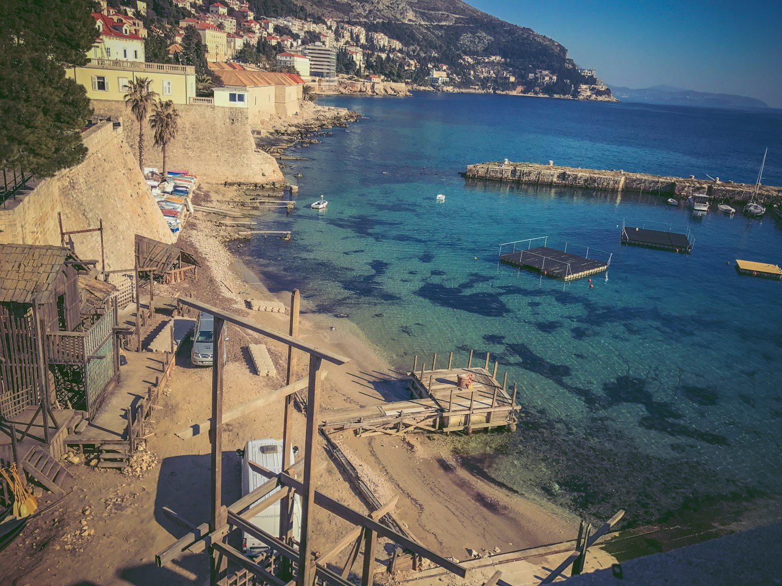 Vista serena della spiaggia con acqua chiara e edifici costieri con un porto e barche da pesca