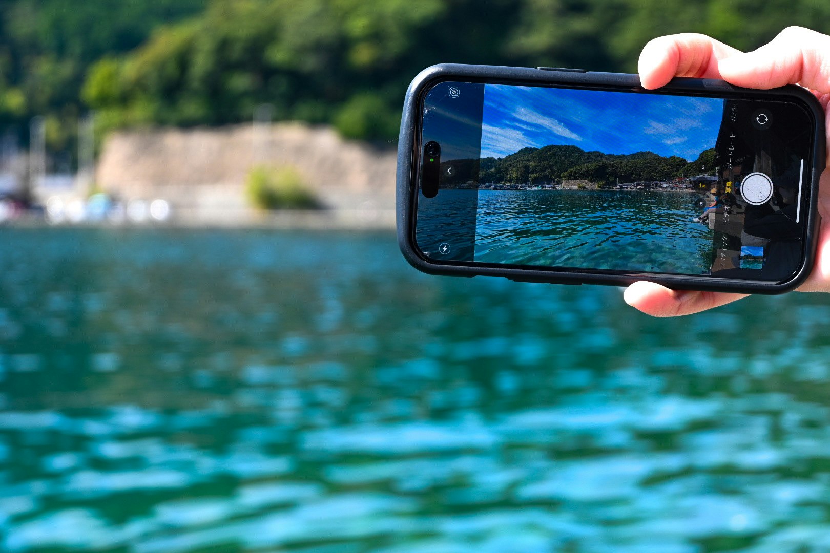 手に持ったスマホで湖の風景を撮影する水辺の景色