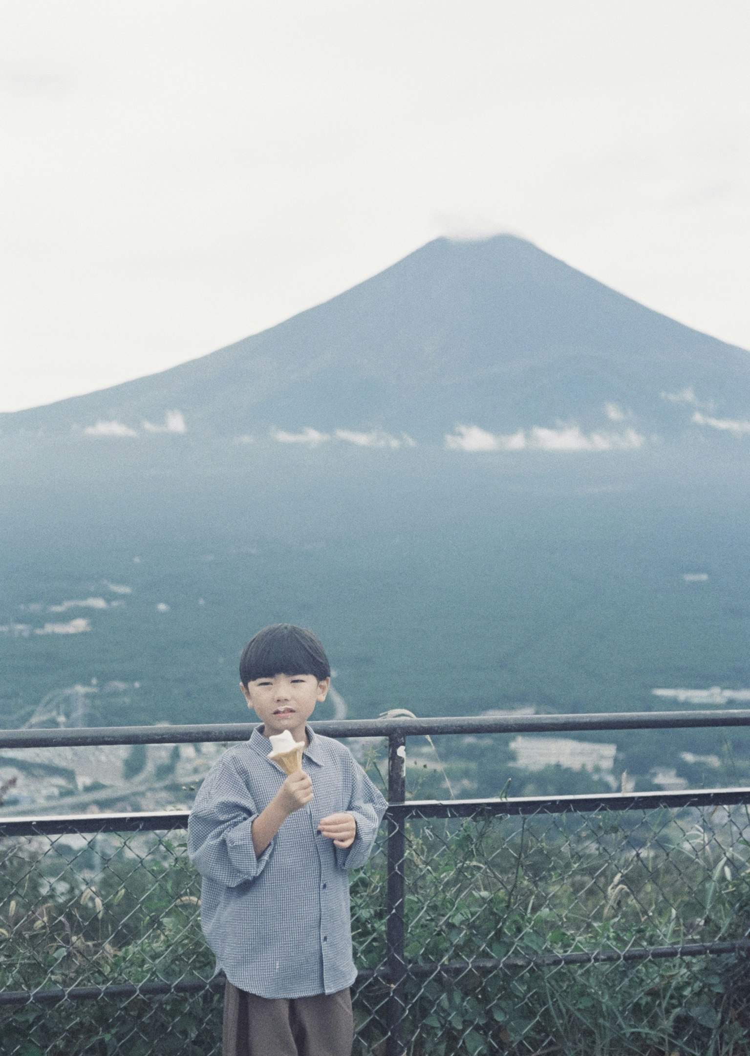 展望台の柵越しに見える山と少年のポーズ