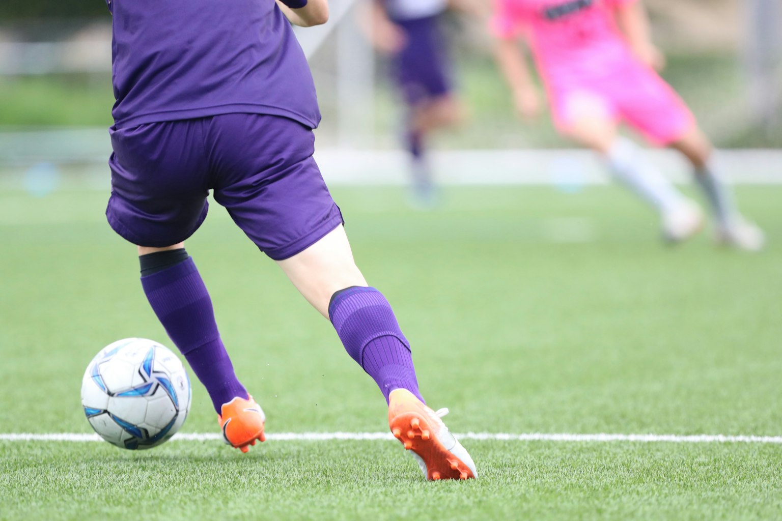 Joueur en uniforme violet courant vers un ballon de football sur le terrain