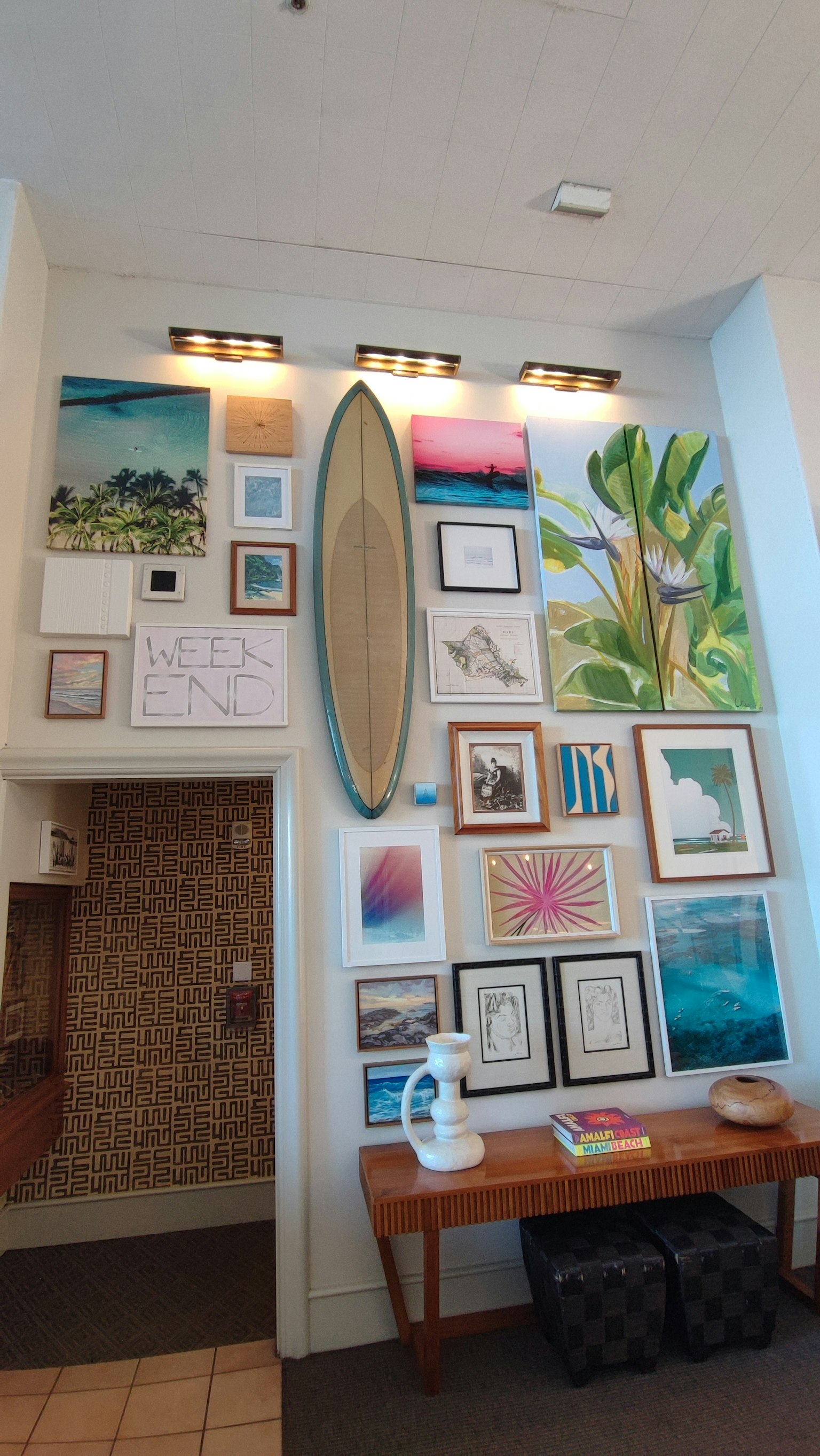 Parete decorata con una tavola da surf e varie opere d'arte incorniciate con un tavolo di legno