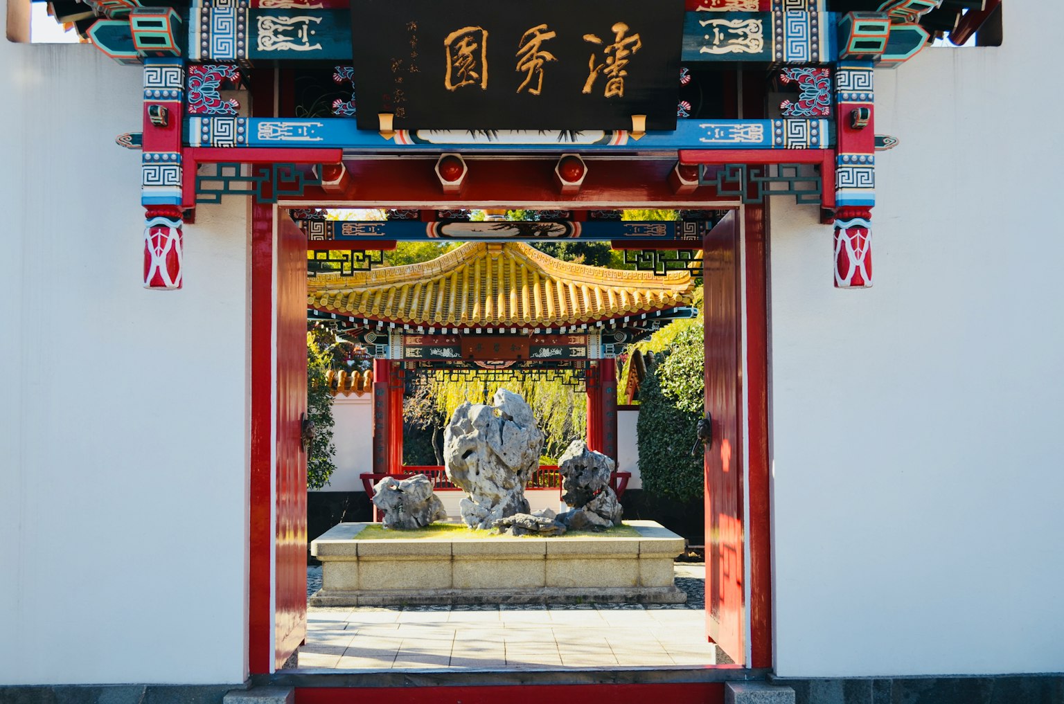 Traditionelles chinesisches Tor mit Blick auf einen überdachten Garten Steinskulpturen in der Mitte Farbige Dekorationen sind auffällig