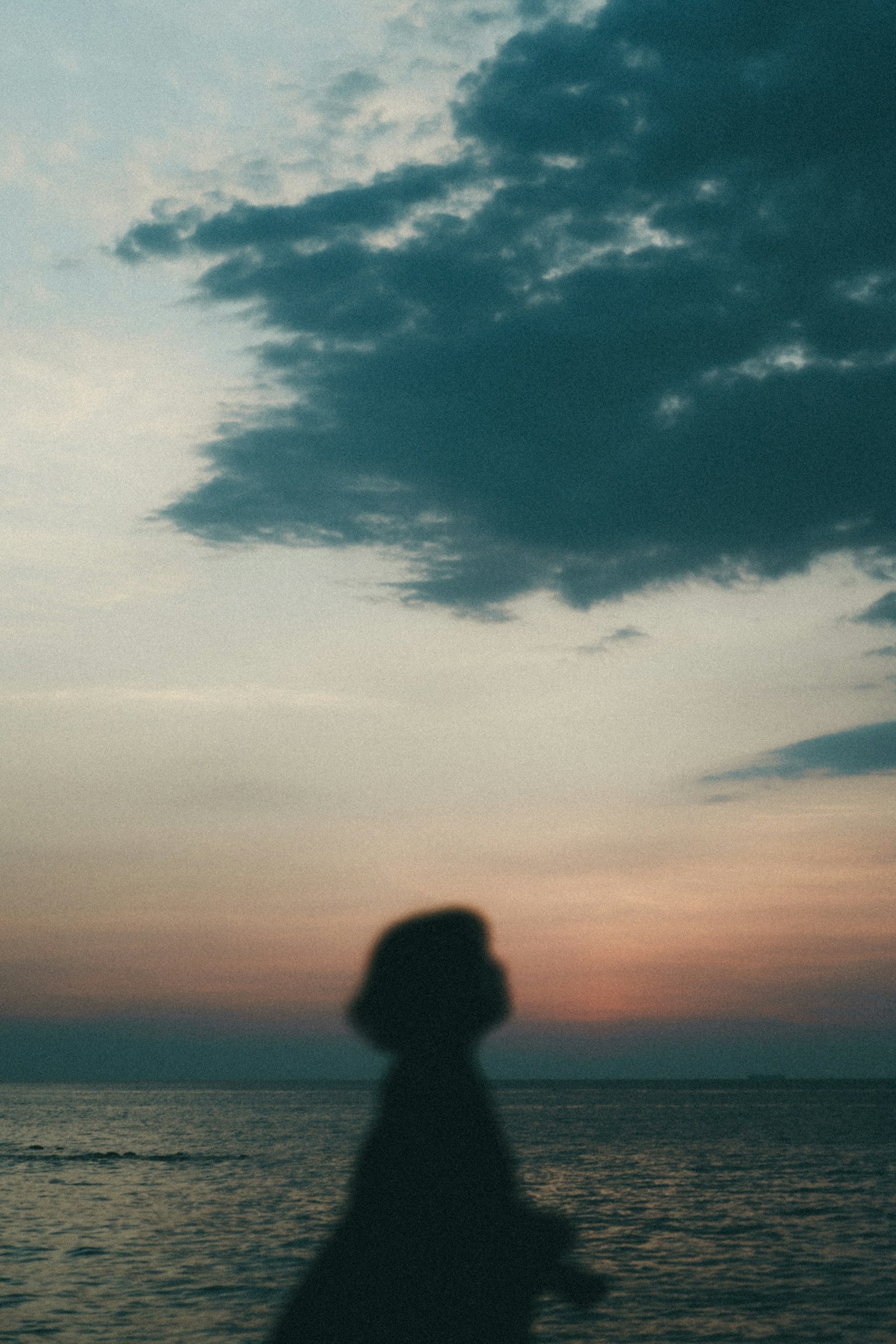 Siluet seseorang yang berjalan di pantai saat matahari terbenam