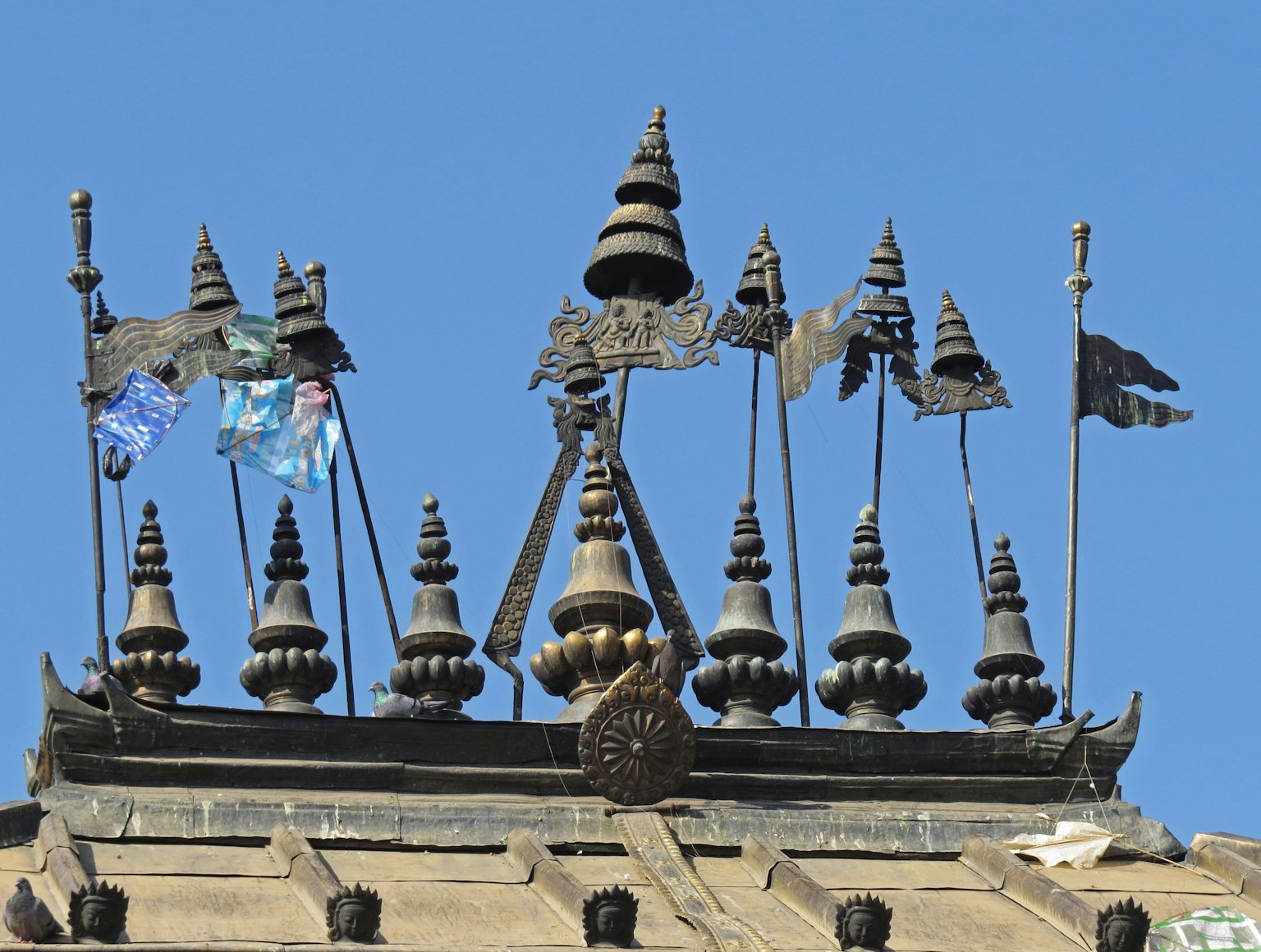 Numerosos pináculos y banderas en la parte superior de un techo de templo bajo un cielo azul
