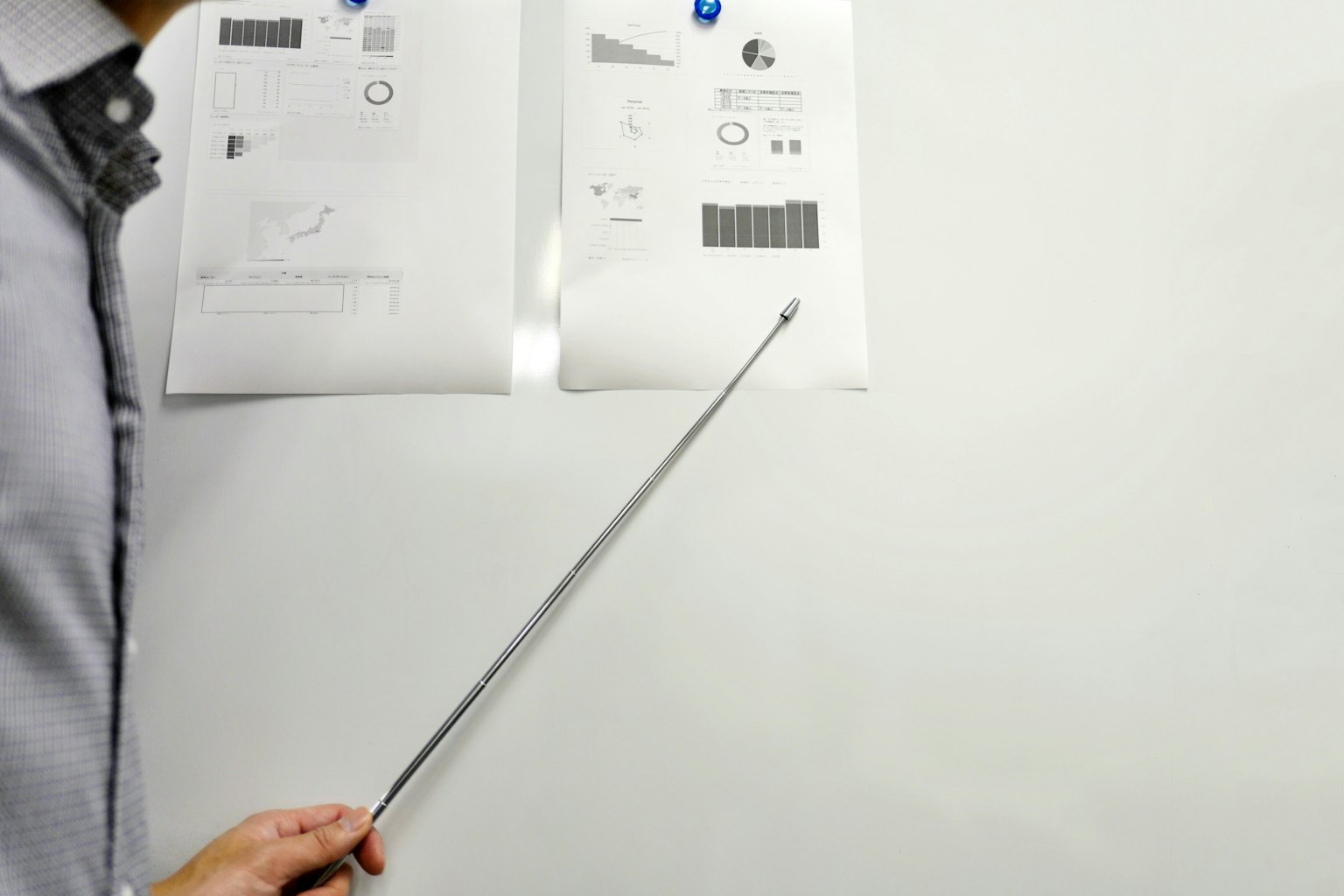 Person pointing at printed materials on a whiteboard during a presentation