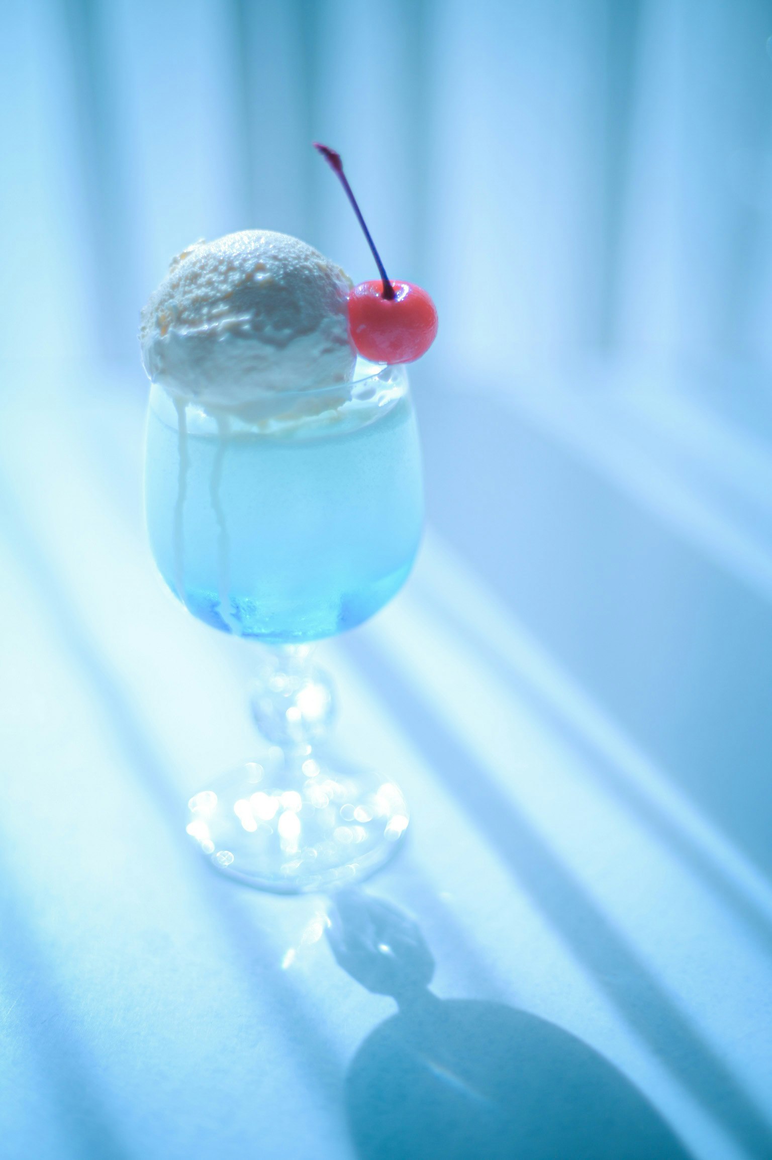 Đồ uống tráng miệng trong ly cocktail màu xanh với kem và một quả cherry trên đỉnh