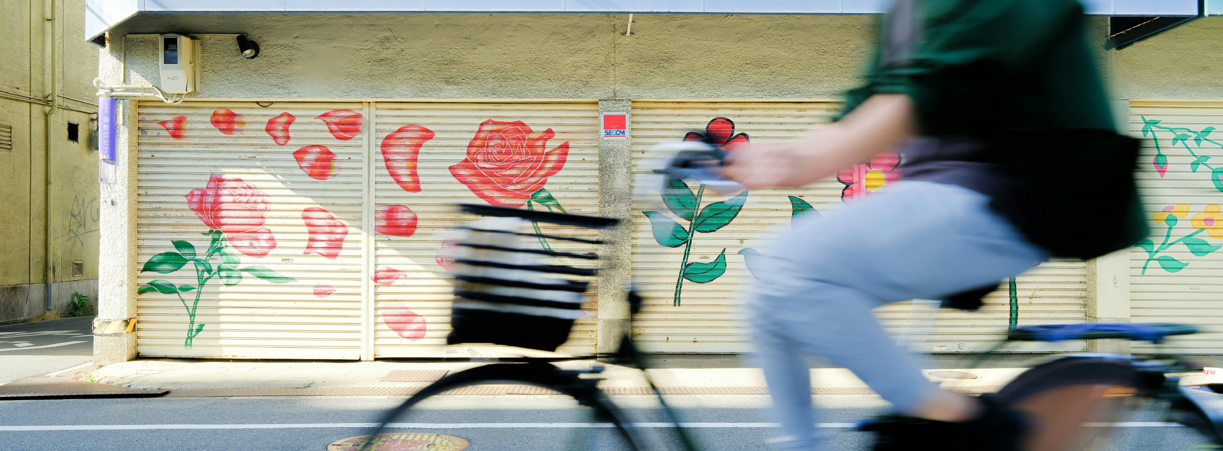 Eine Person fährt mit dem Fahrrad an einem Rolltor mit Blumen-Graffiti vorbei