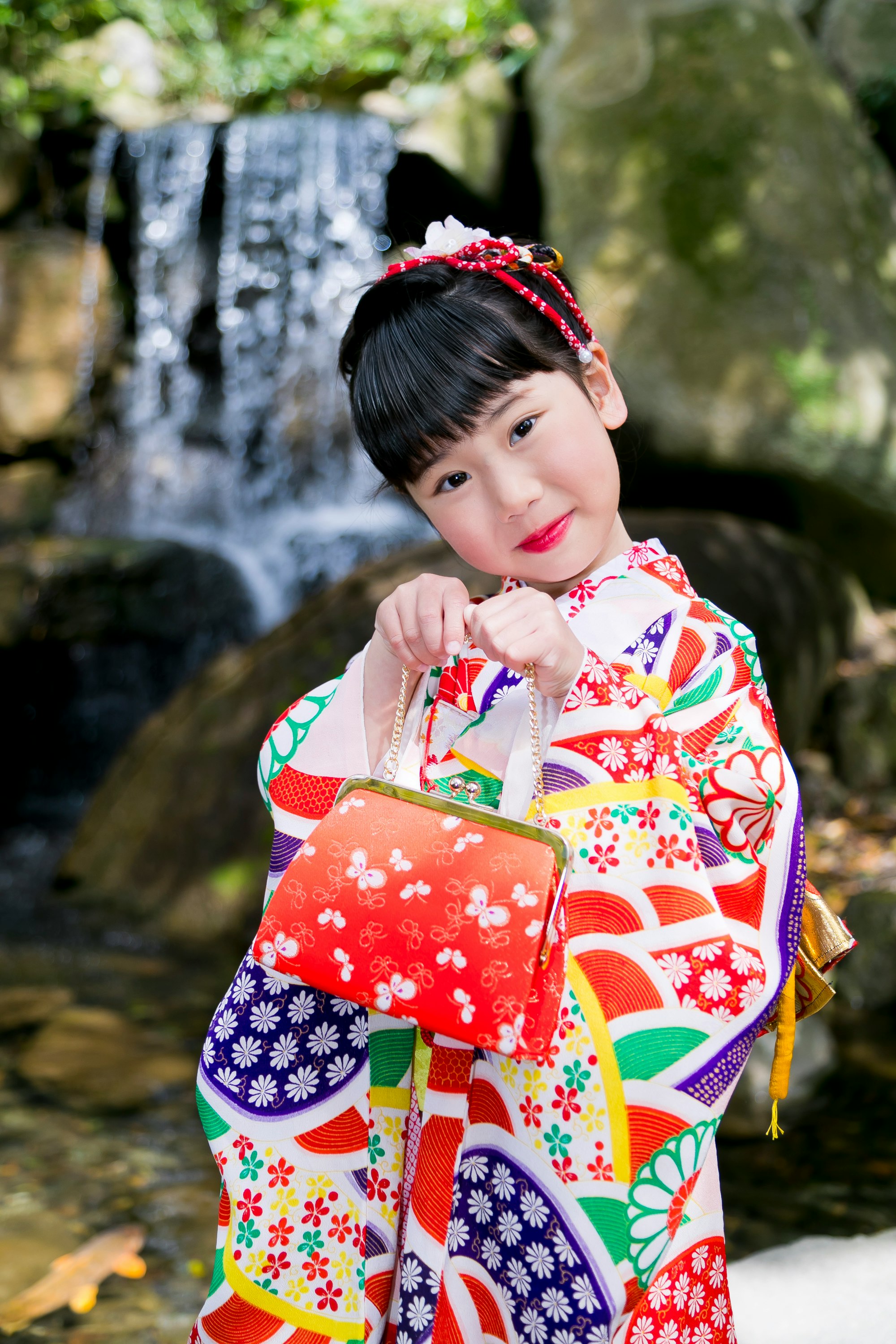 滝のそばで赤い着物を着た子どもの七五三姿