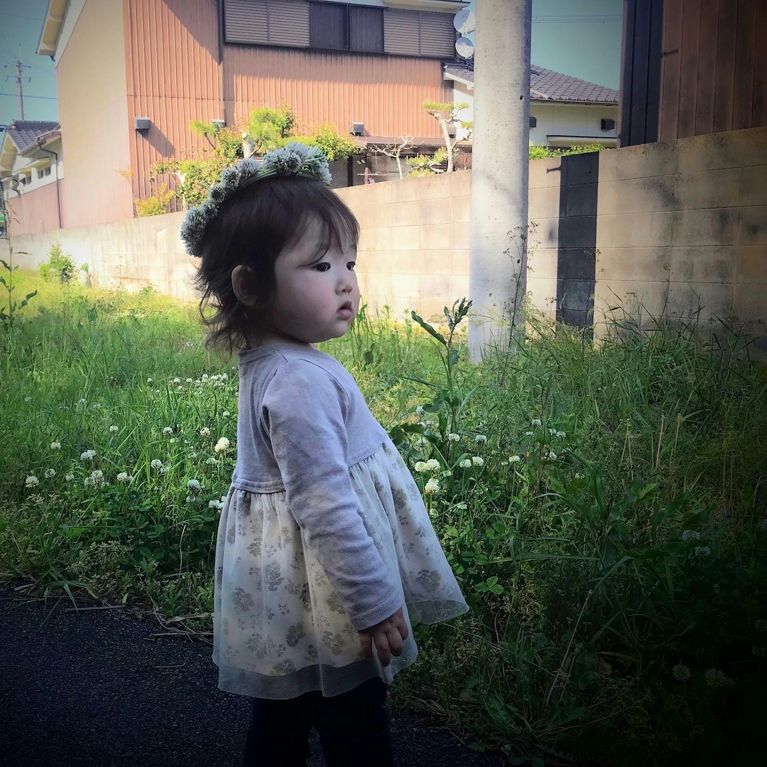 Une petite fille portant une couronne de fleurs se tenant à côté d'un chemin entouré d'herbe verte