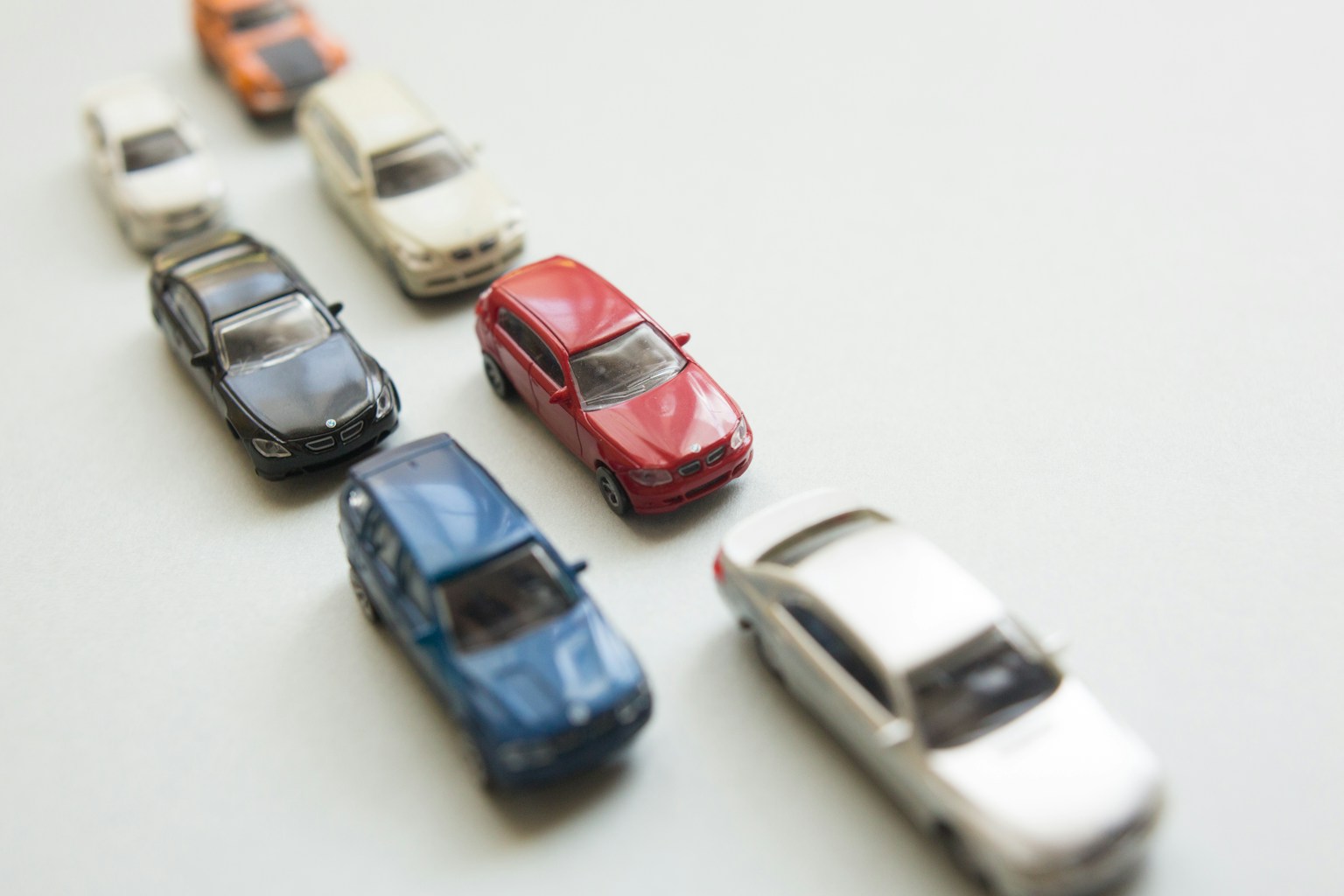 Une rangée de voitures miniatures sur un fond blanc avec une voiture rouge au centre entourée de voitures bleue, noire, blanche et orange