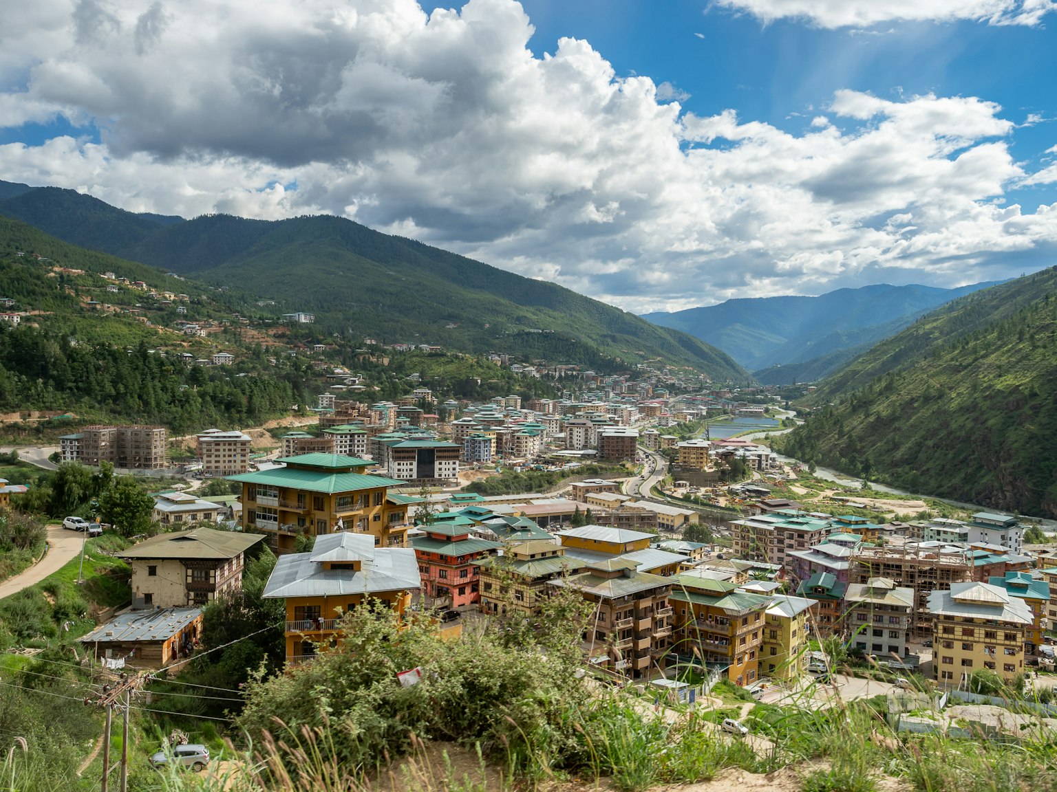 Vue de Thimphou au Bhoutan entourée de montagnes vertes ciel bleu et nuages blancs