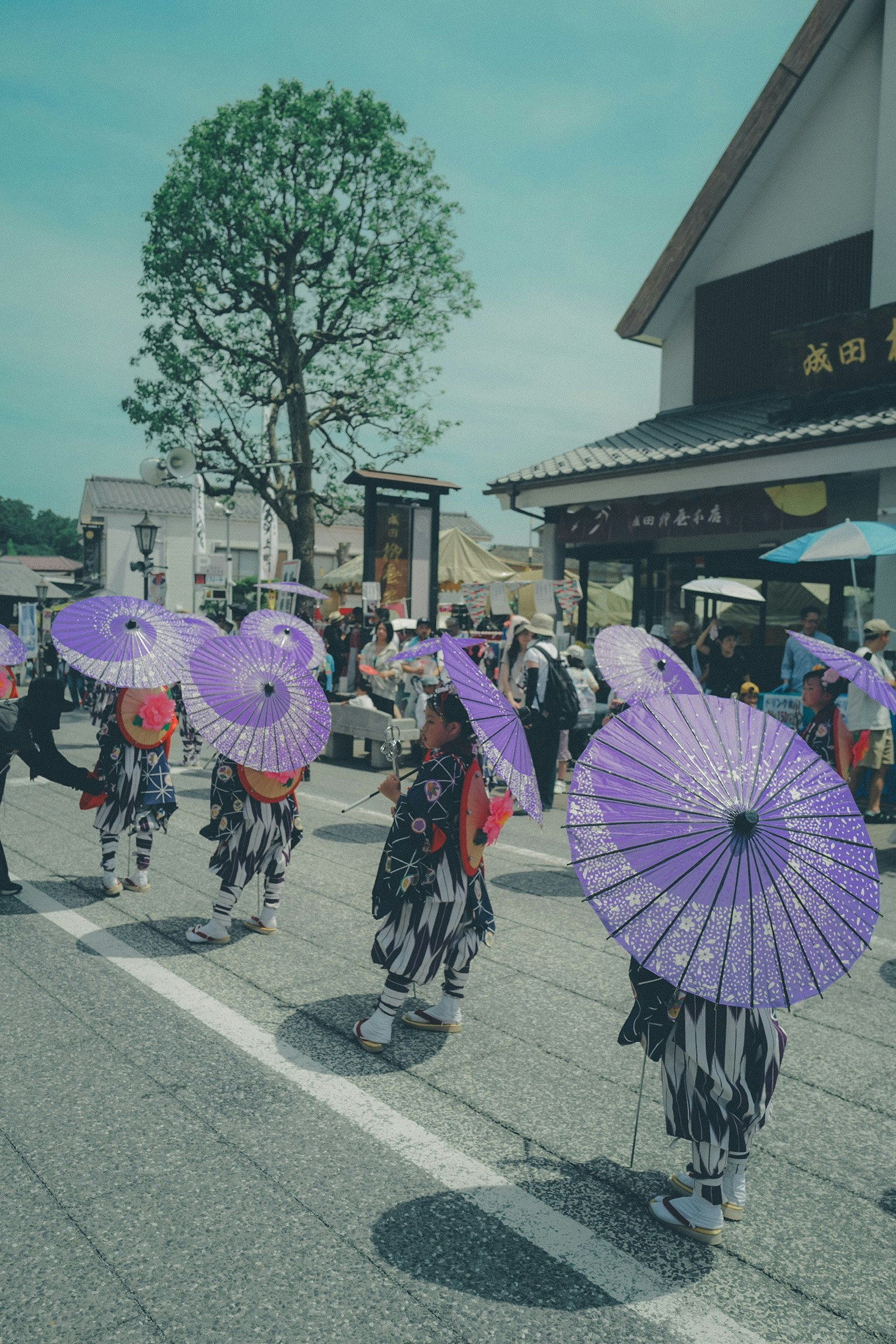 和傘を持つ人々が並ぶ屋外のイベント会場の通路