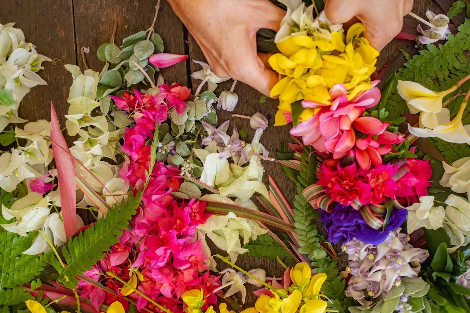 Mani che sistemano una varietà di fiori colorati su una superficie di legno