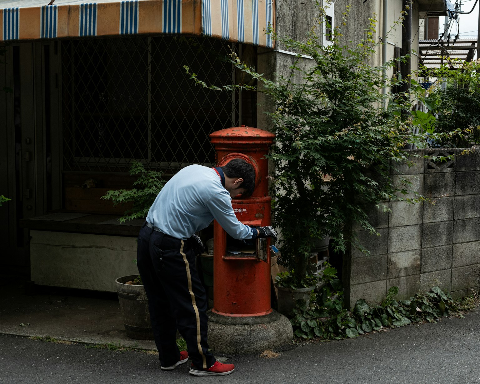 Un homme déposant une lettre dans une boîte aux lettres rouge dans une scène de rue