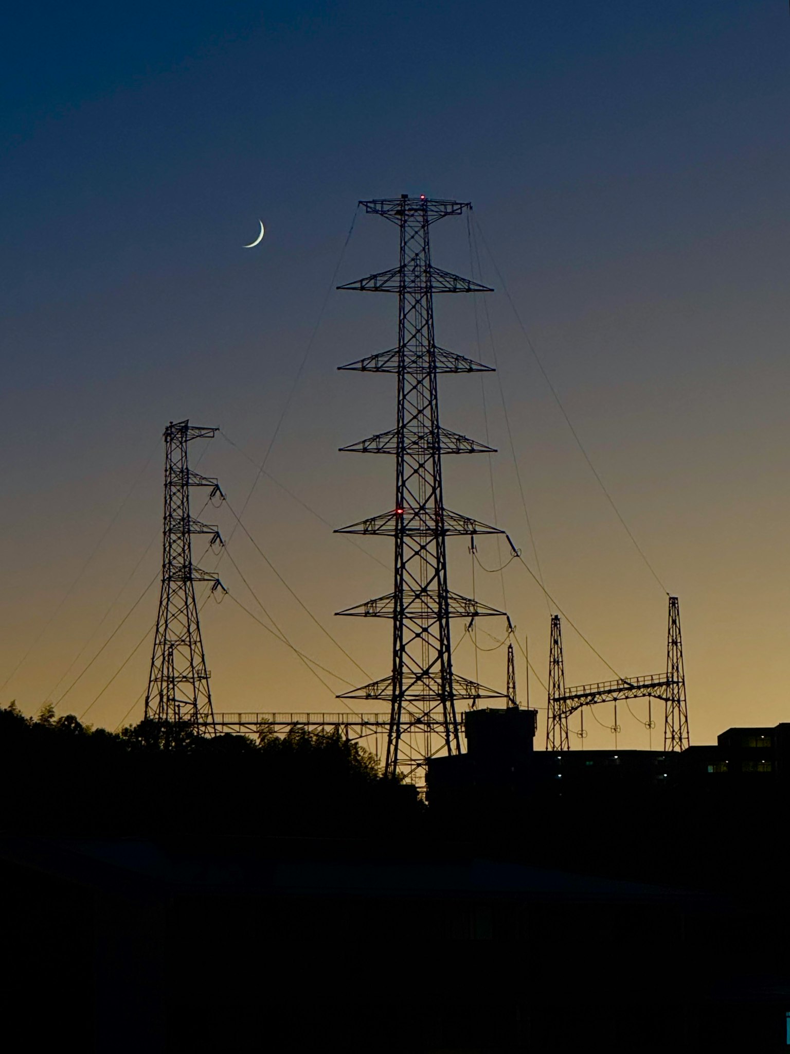 夕暮れ時の電力塔と細い月が見える風景