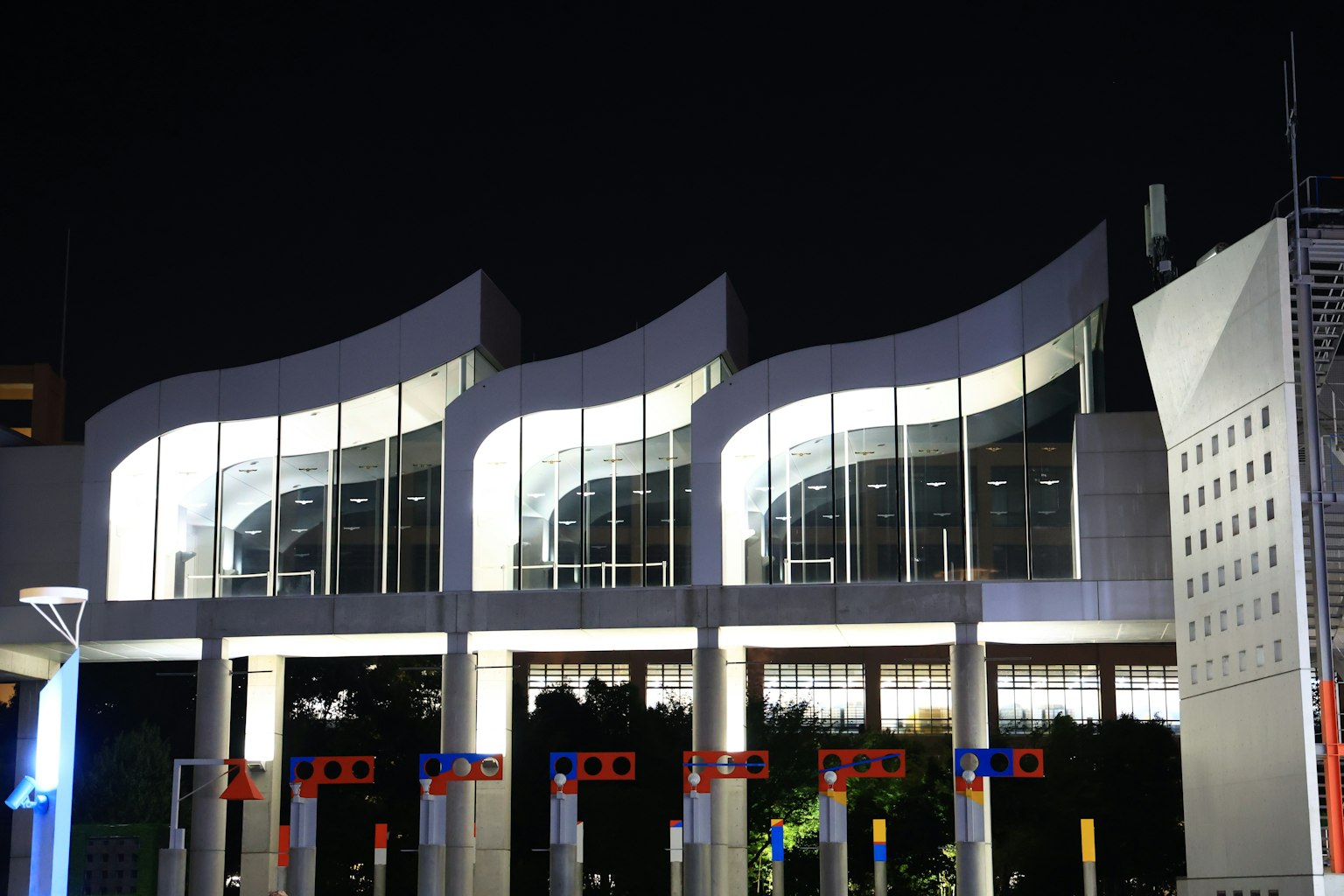 Fachada de un edificio moderno con tres techos en forma de ola iluminados por la noche