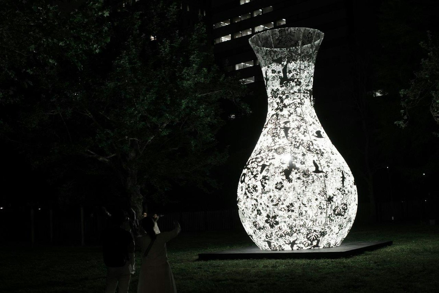 Grande installation artistique en forme de vase illuminé dans un parc la nuit