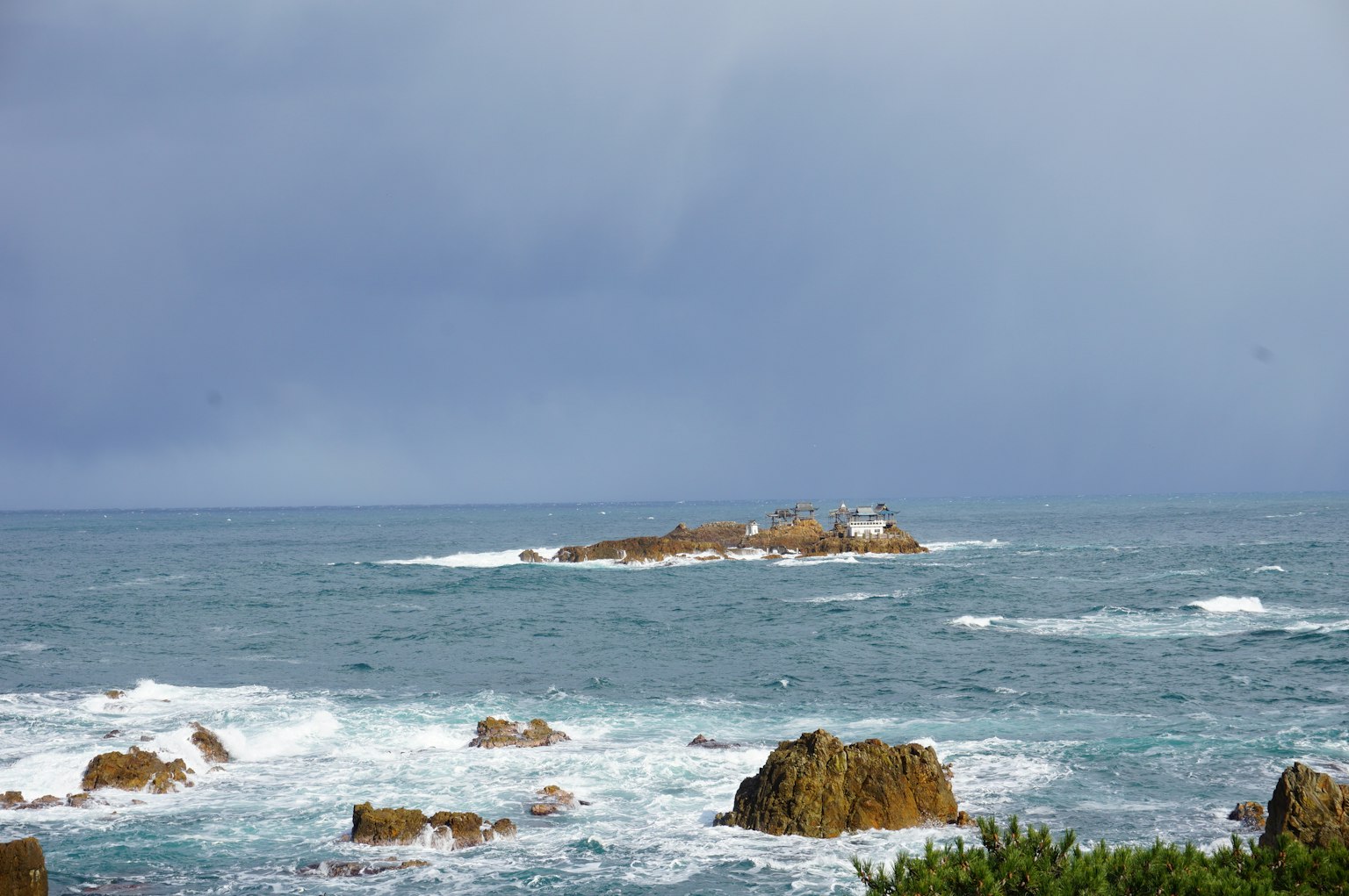 Vista dell'oceano blu con una costa rocciosa e un'isola piccola