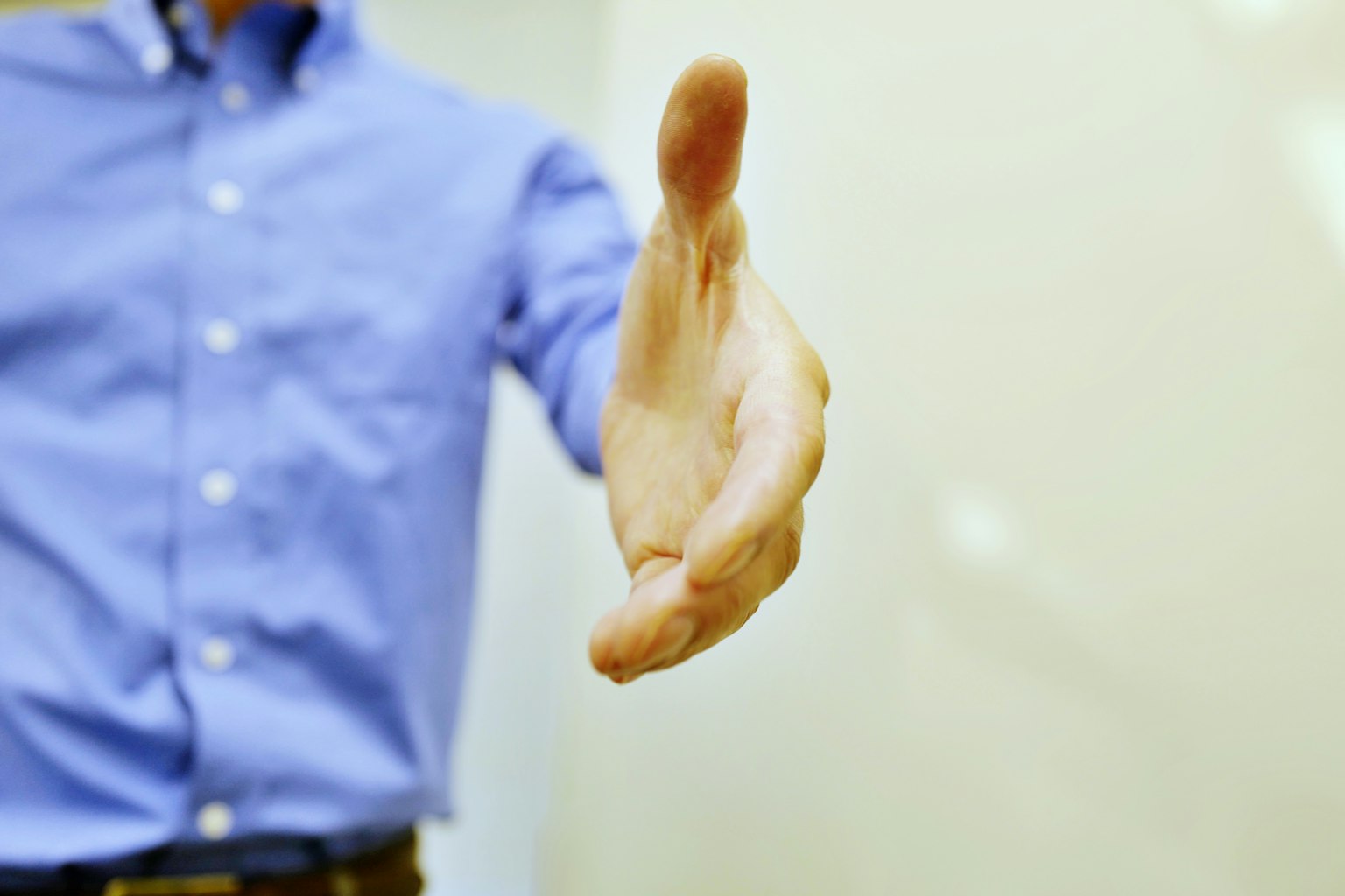 La mano de un hombre extendida en saludo vistiendo una camisa azul
