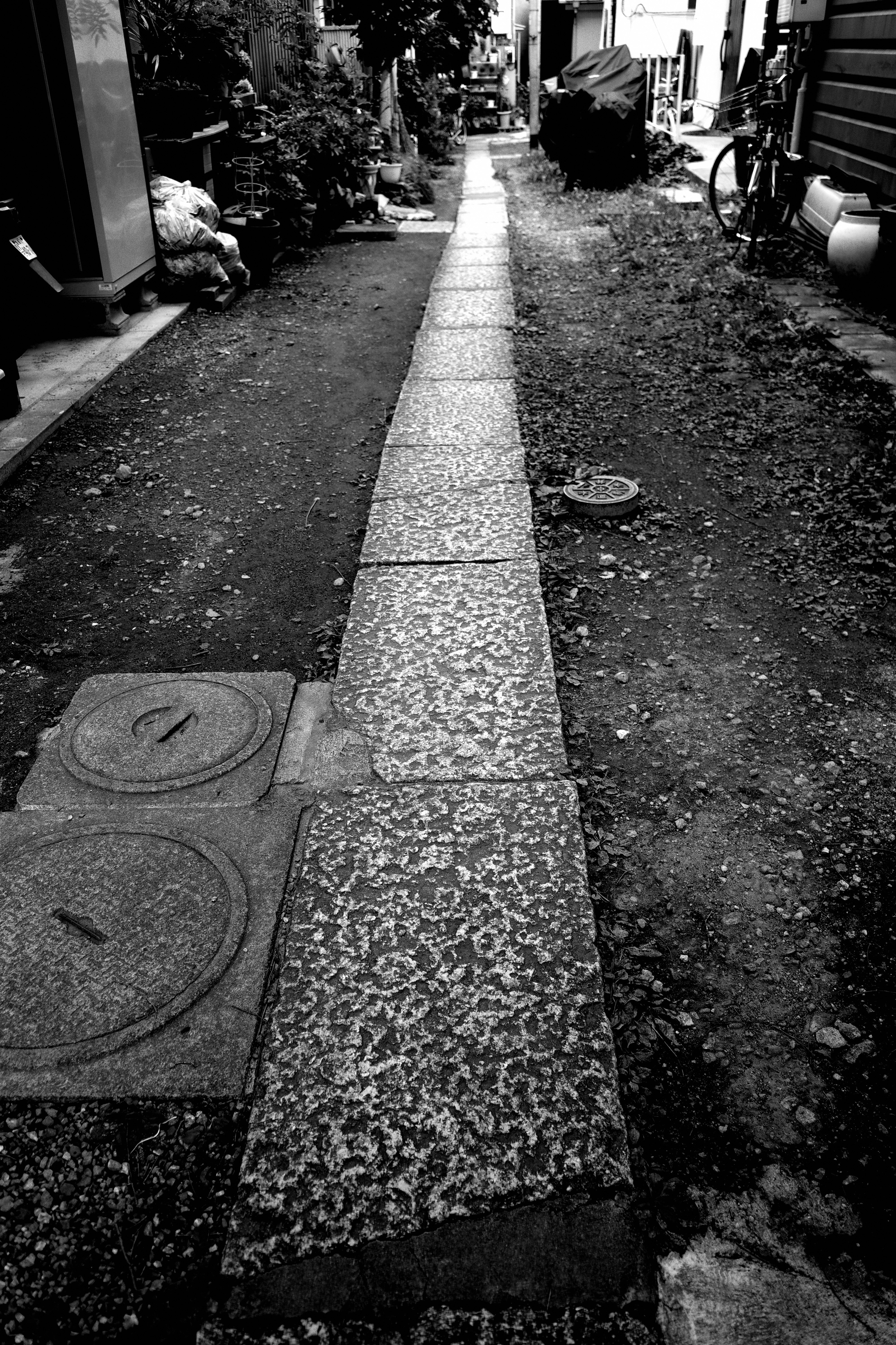 狭い路地に沿った石畳の歩道と周囲の雑草やゴミ