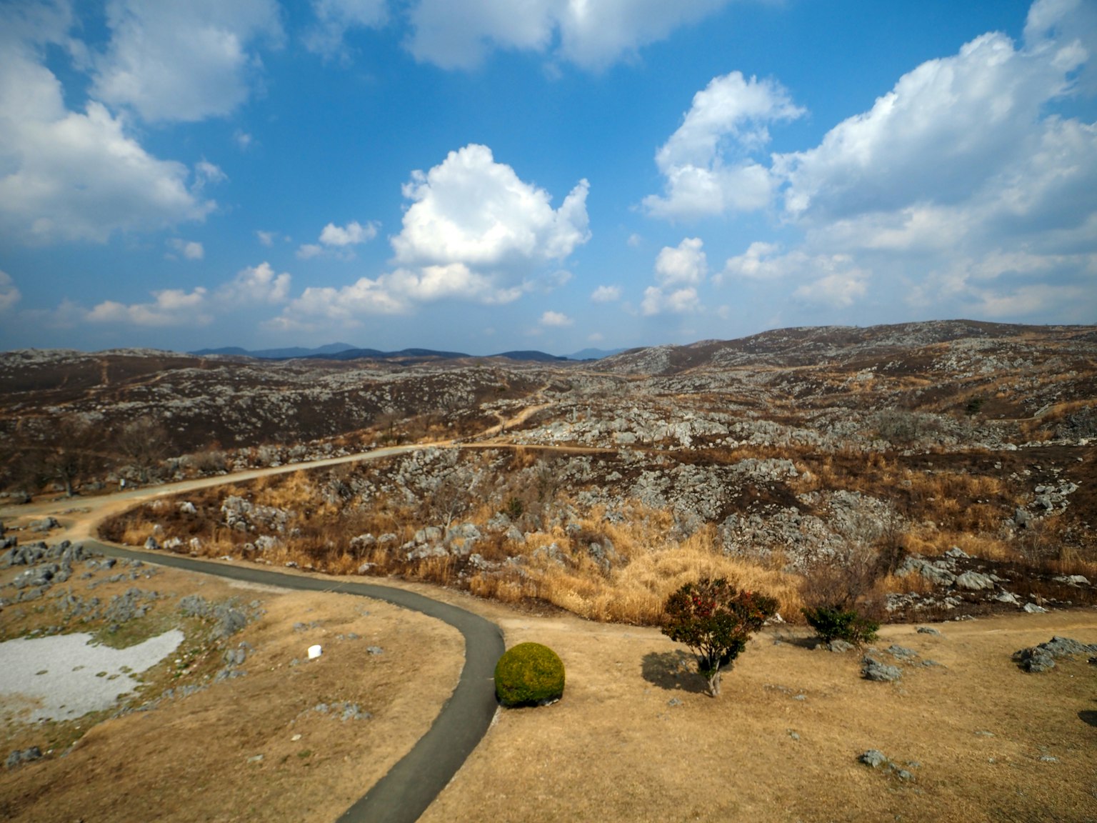 Pemandangan kering dengan bukit bergelombang dan langit biru, dengan rumput jarang dan batu-batu tersebar
