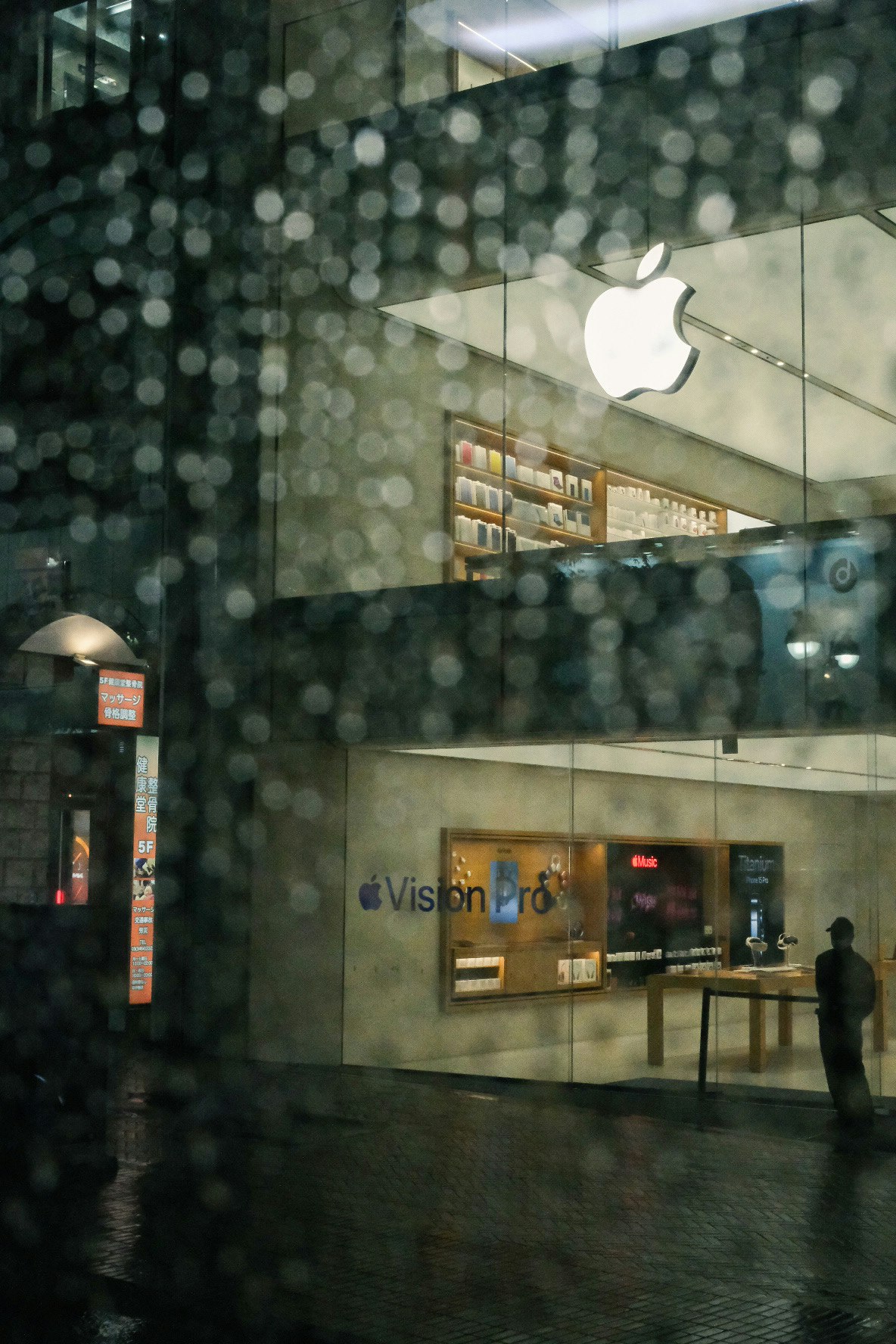 雨の夜にガラス越しのAppleロゴが見える店頭