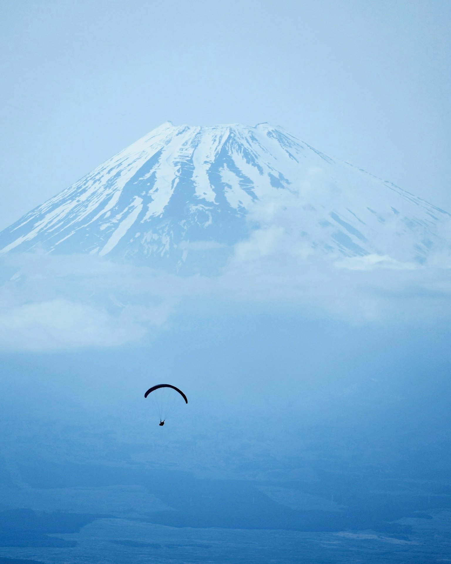 Un parapendio che vola sotto una montagna coperta di neve in un cielo azzurro