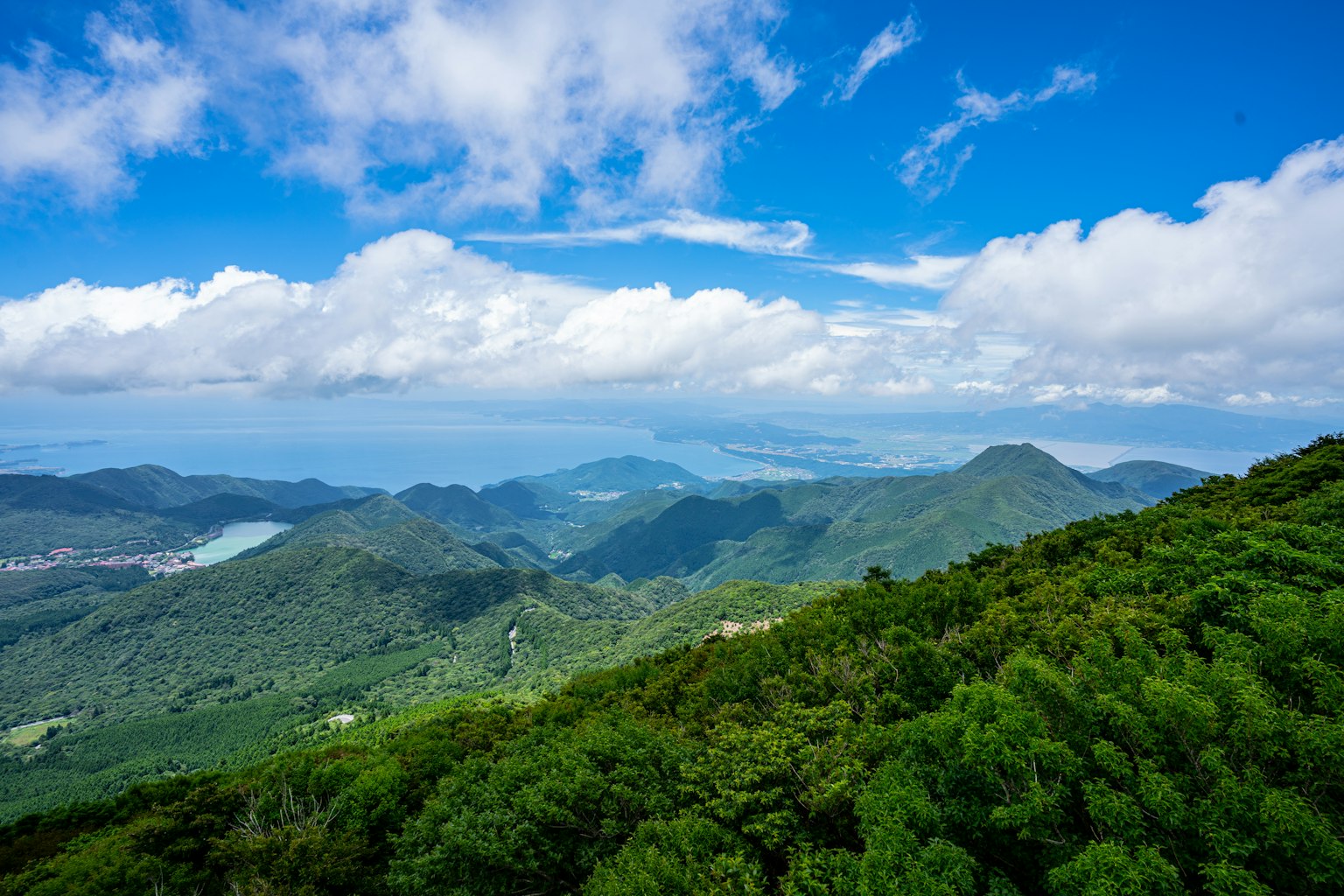 Berglandschaft mit blauem Himmel und weißen Wolken grünen Wäldern und entferntem Meer