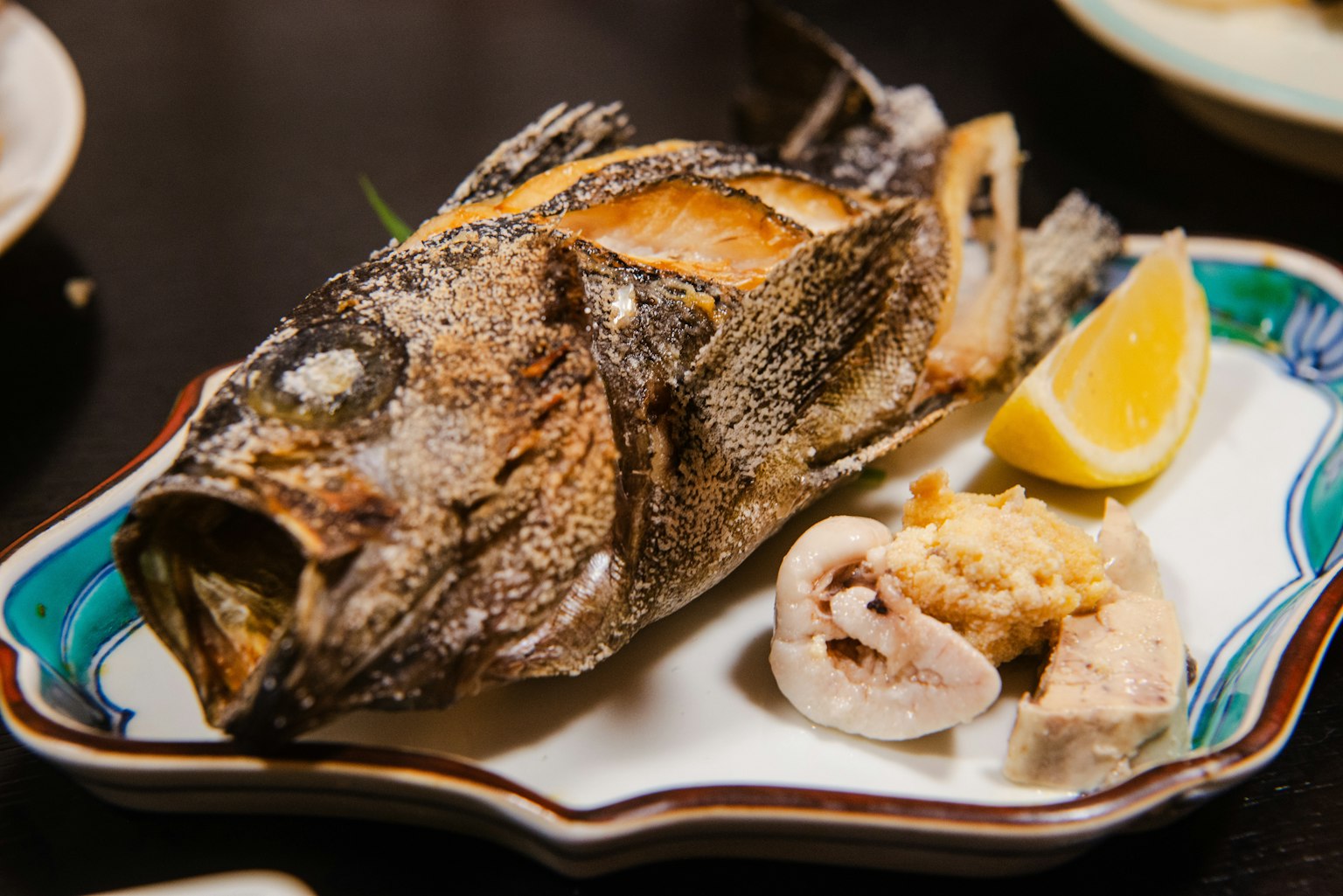 Grilled fish served on a plate with lemon and condiments