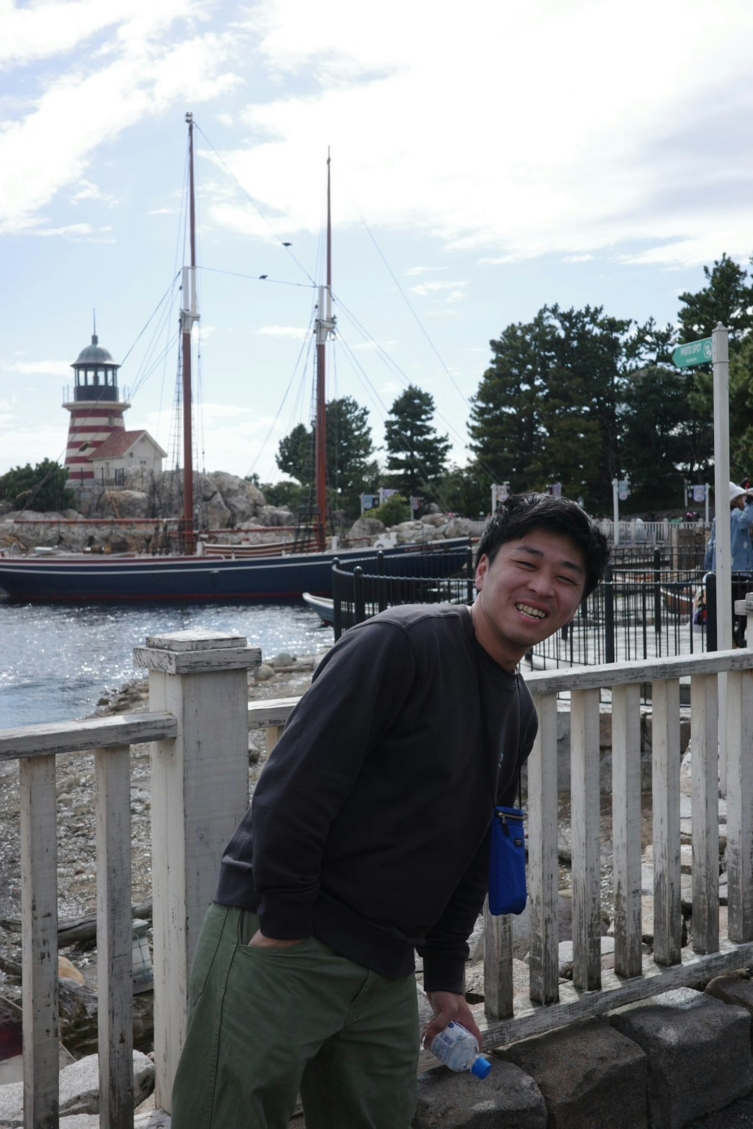 Homme souriant devant un phare et des voiliers au bord de la mer
