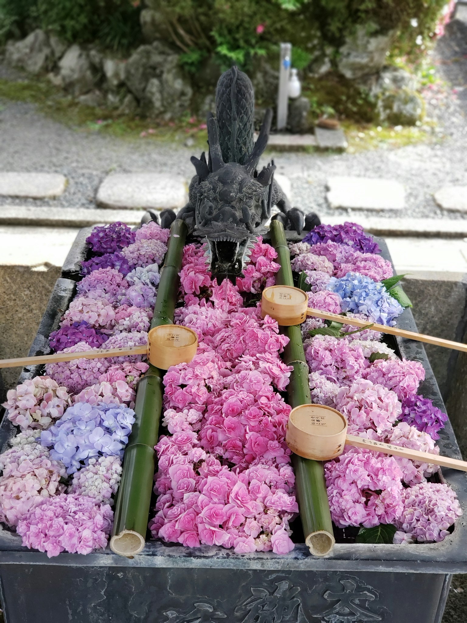 Un bassin d'eau décoré de fleurs avec des louches en bambou et une statue d'animal noir au-dessus