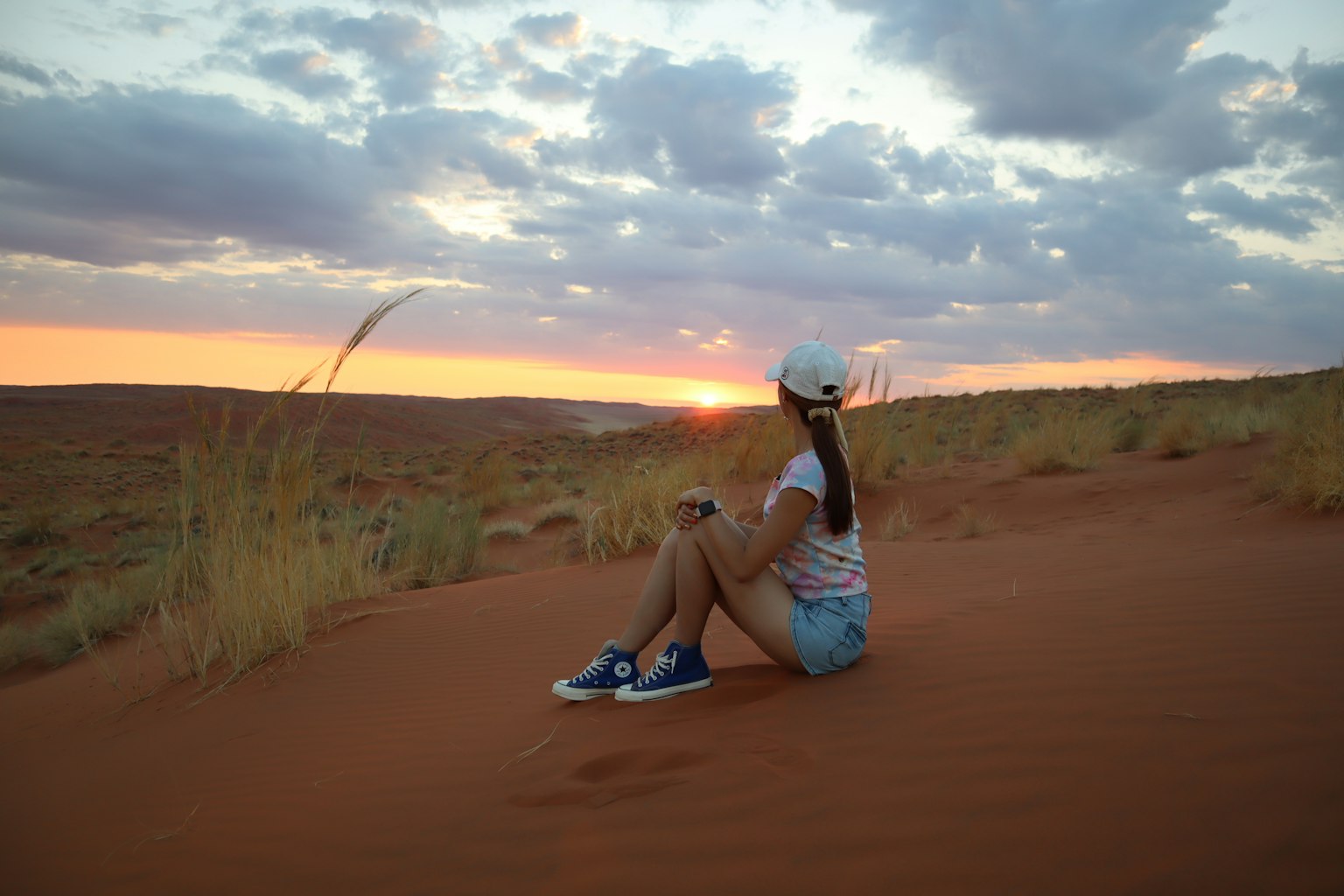 Une femme assise sur une dune de sable regardant le coucher de soleil