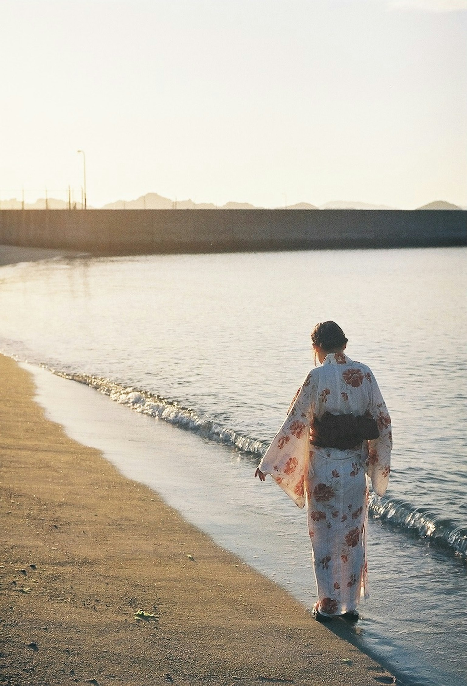 身著和服的女性在沙灘上漫步，背景是夕陽