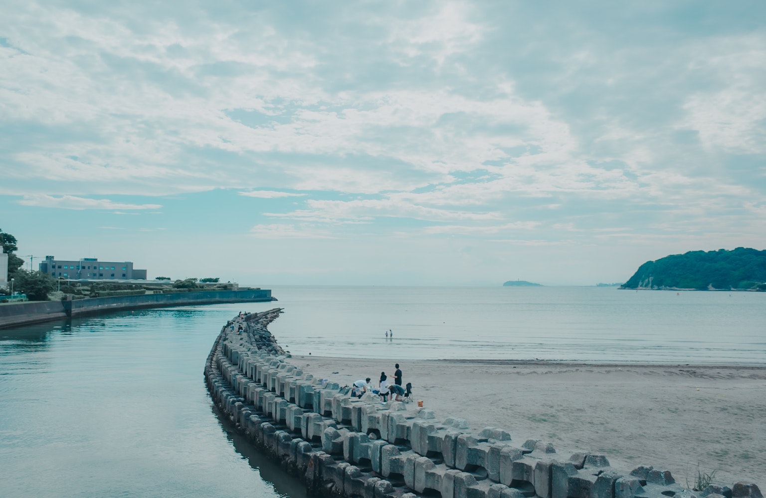 Pemandangan laut yang tenang dengan langit biru pemecah gelombang di sepanjang pantai dan orang-orang
