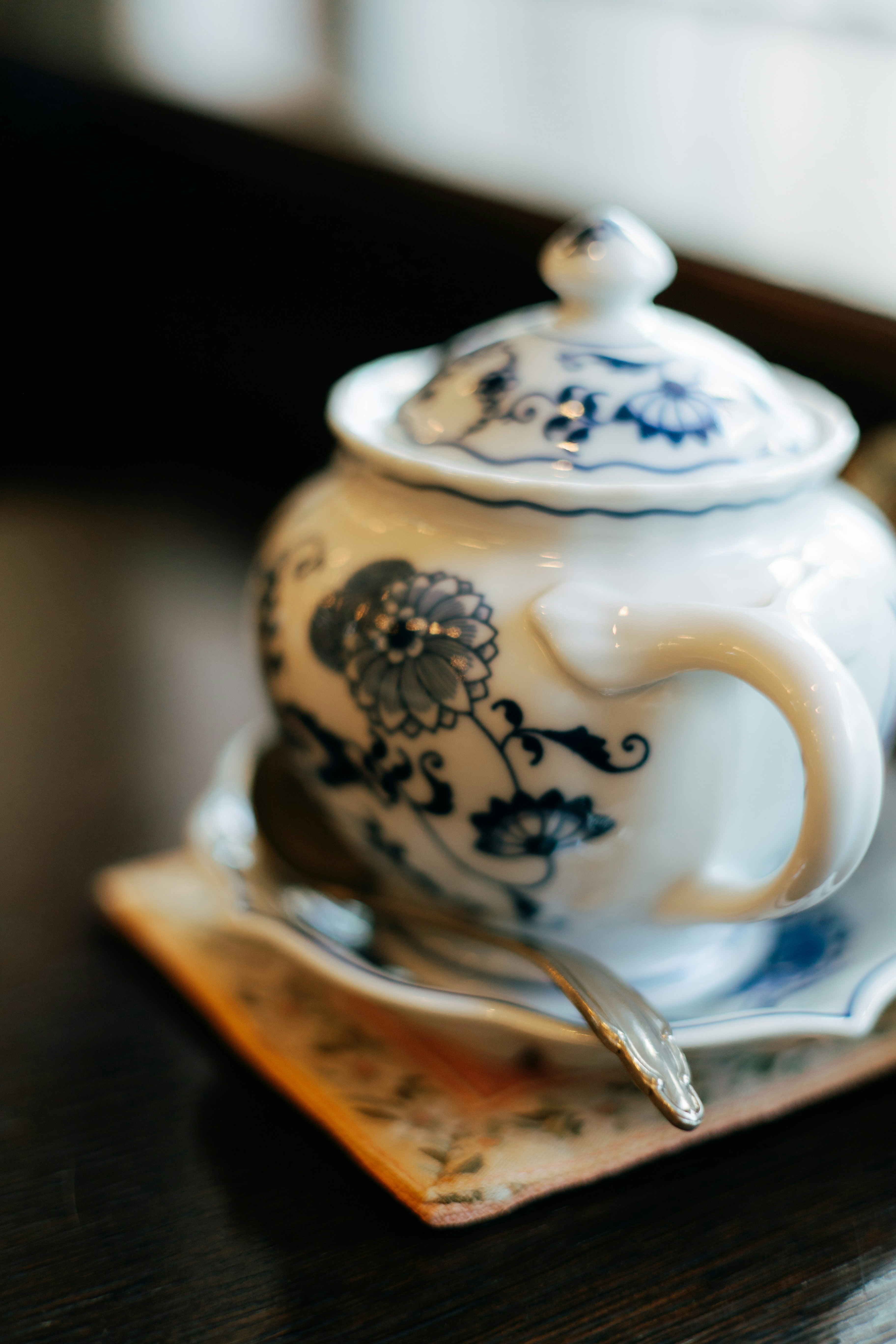 Théière blanche avec des motifs floraux bleus placée sur une table avec une petite soucoupe et une cuillère