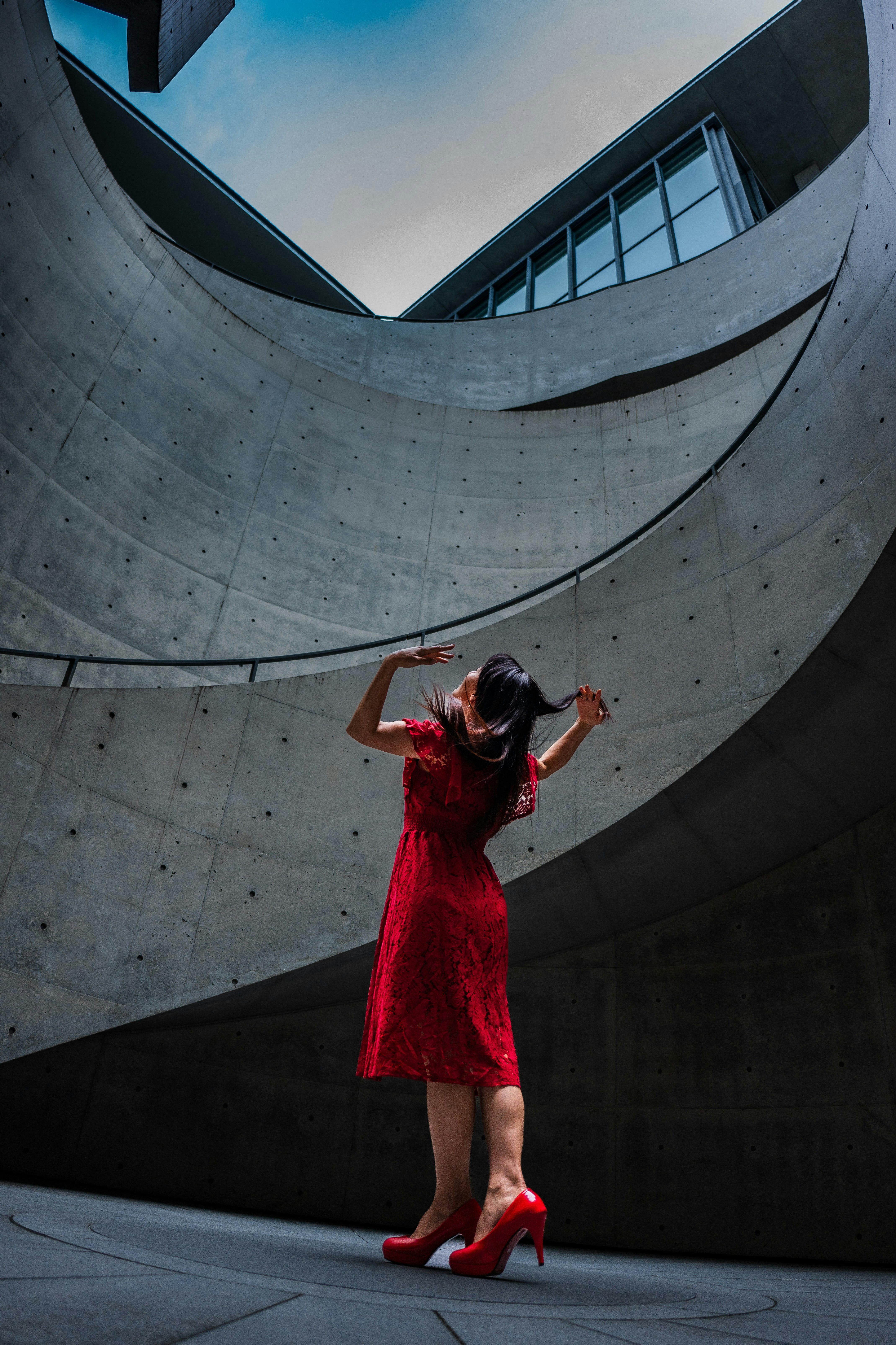 曲線的なコンクリート建築の前で赤いドレスのポートレート