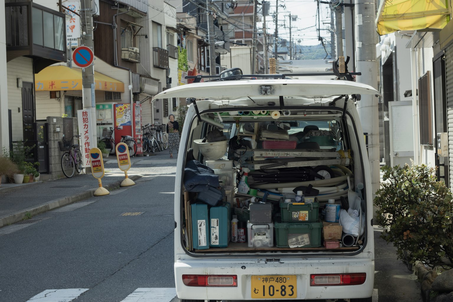 A white van parked on a narrow street filled with various tools and supplies in the back