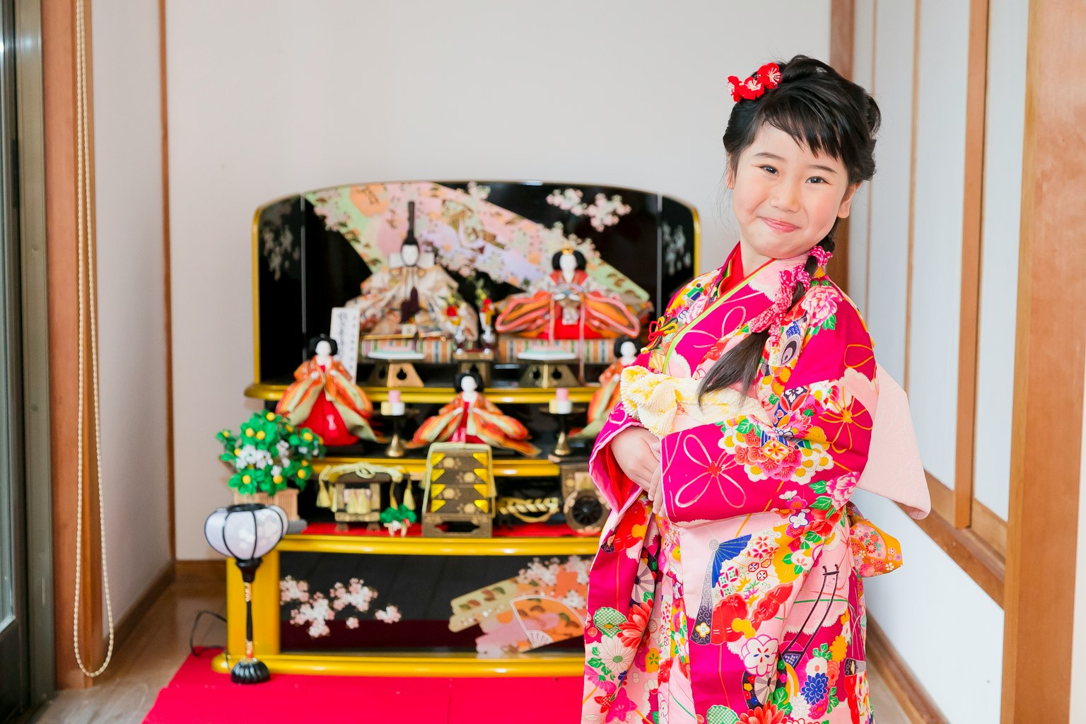 Seorang gadis berpakaian kimono tersenyum di depan boneka hina