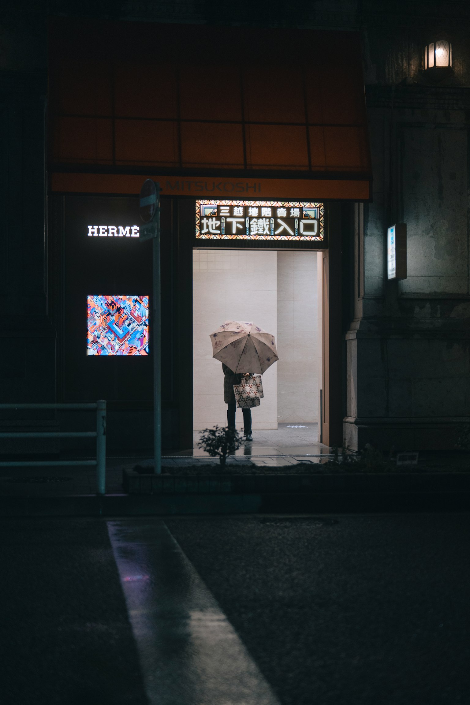 Una persona con un ombrello davanti a un negozio Hermès di notte