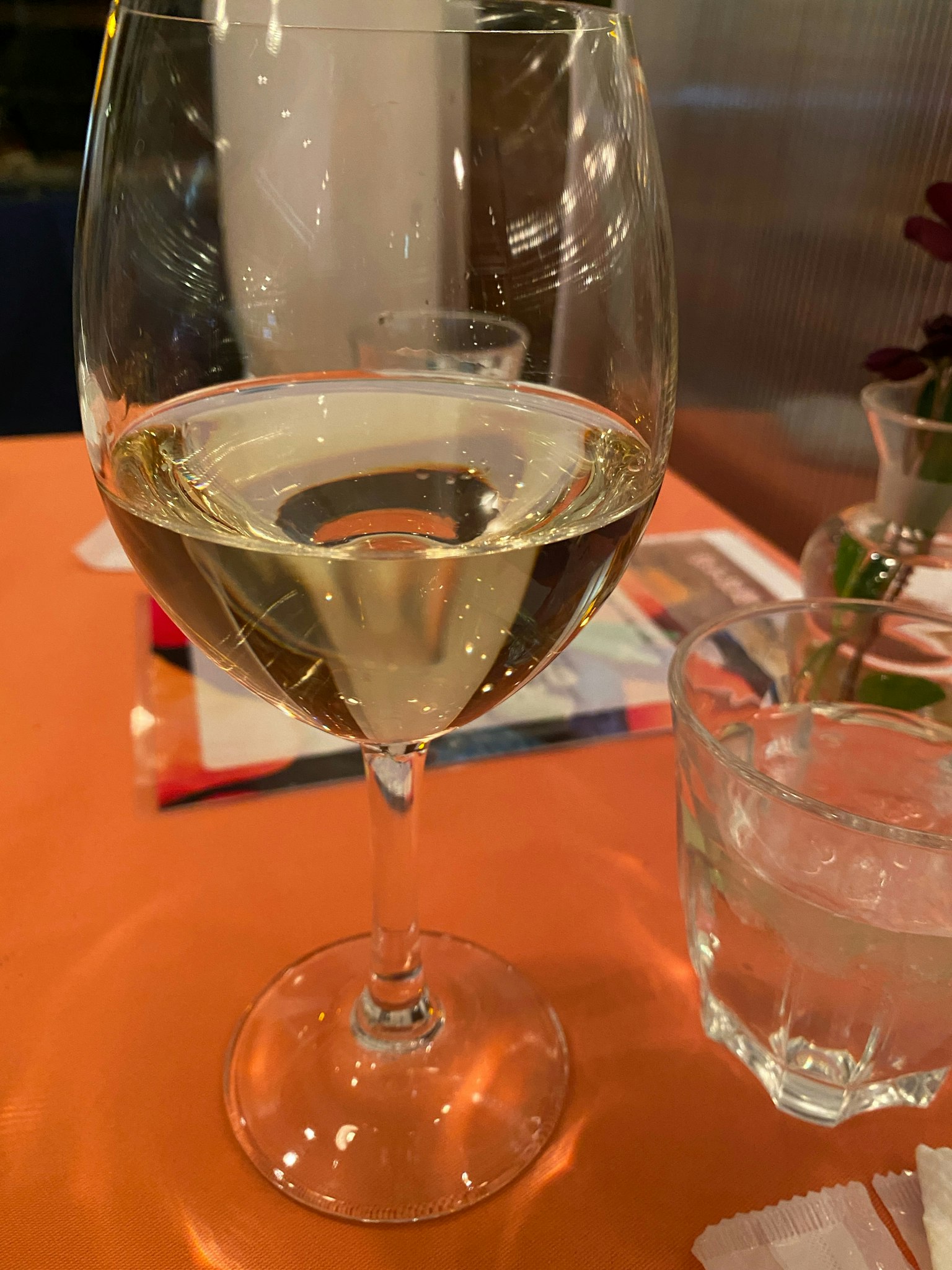 Un vaso de vino blanco junto a un vaso de agua sobre una mesa naranja