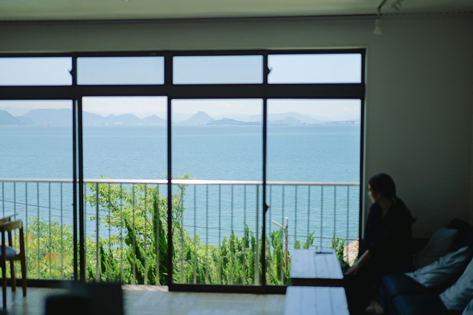 Chambre avec de grandes fenêtres donnant sur une belle vue sur la mer et une personne assise à côté