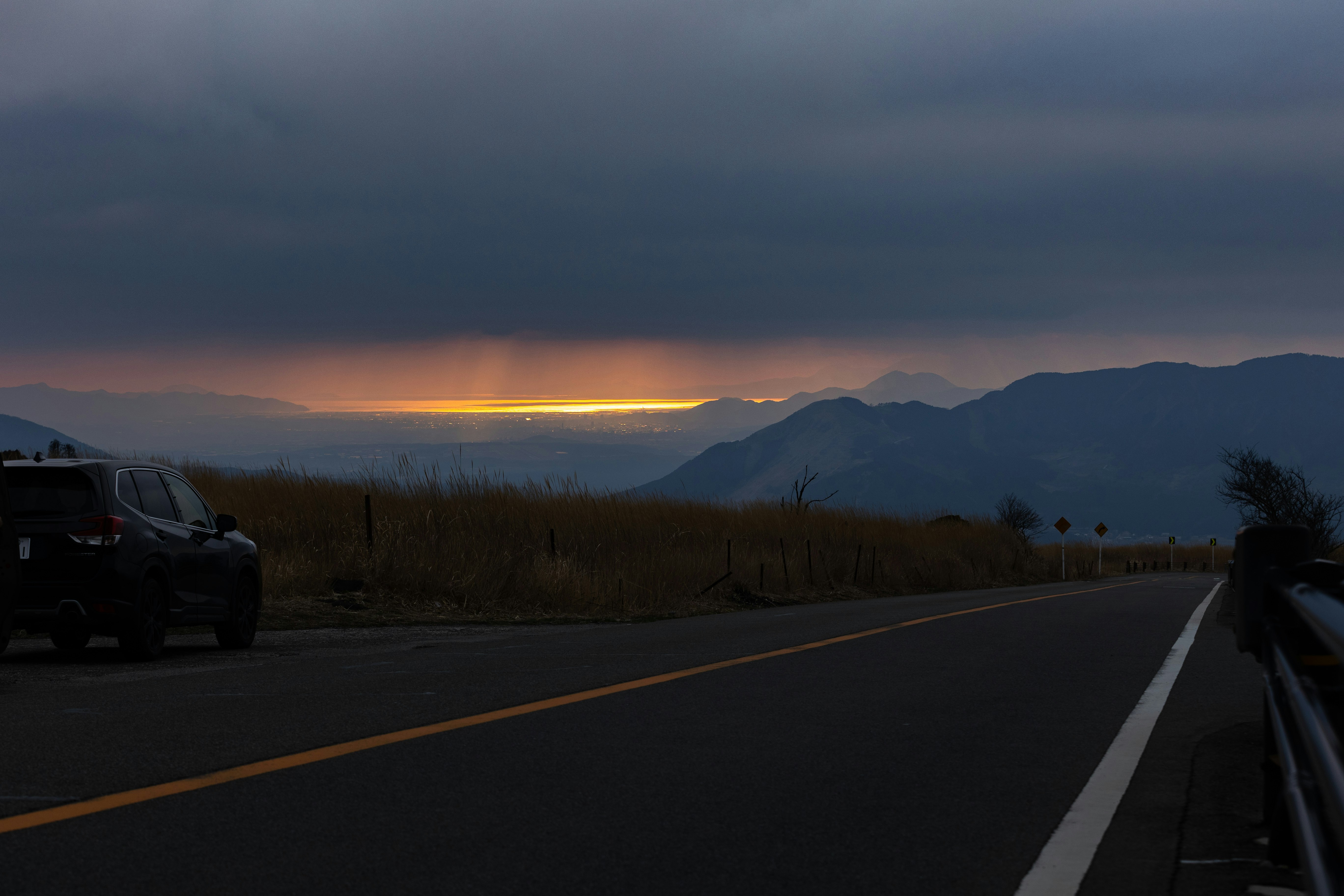 夕暮れの山並みと湖を望む田舎道の風景