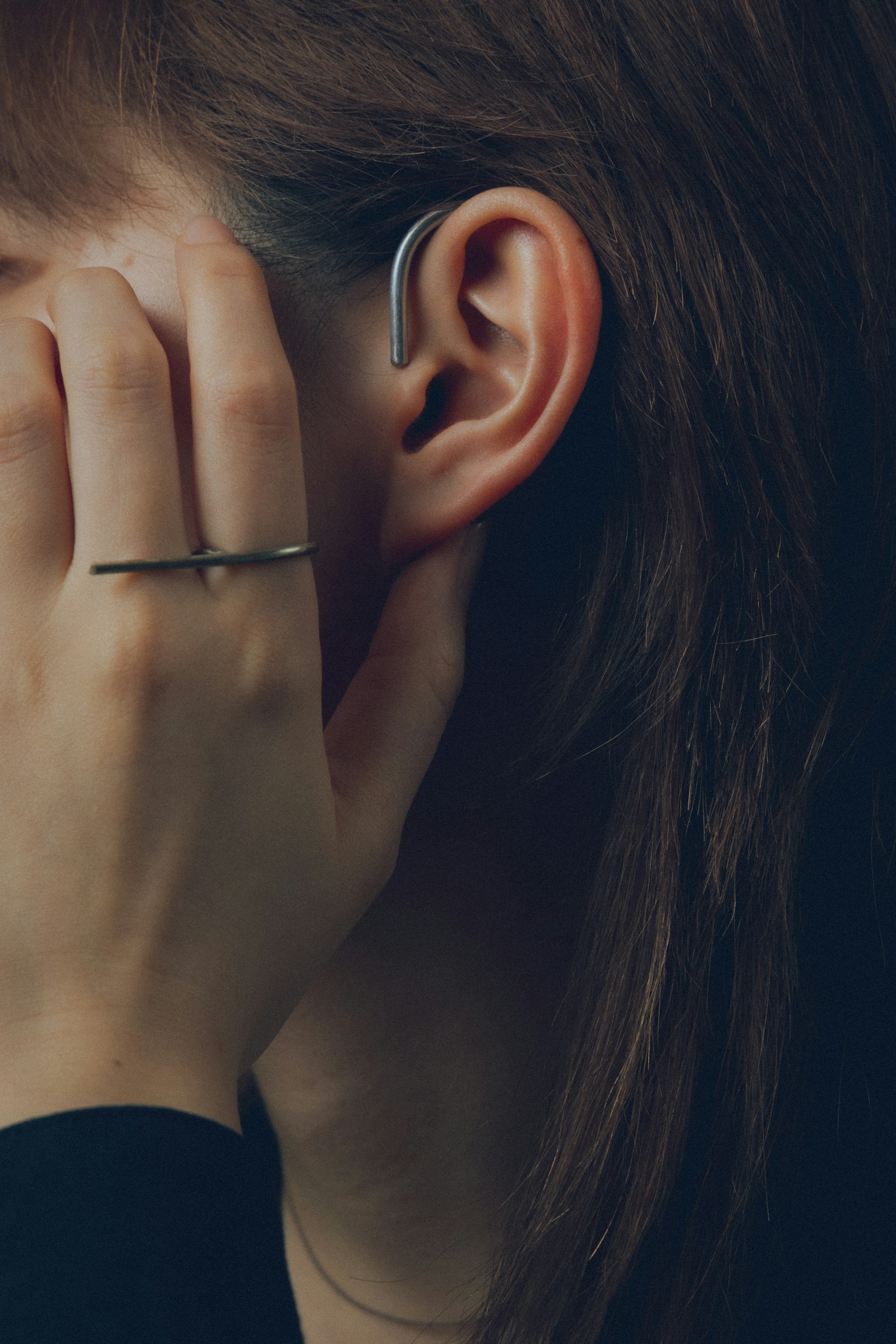 Profile of a woman partially obscured by her hand wearing a hearing aid on her ear with a simple ring on her finger